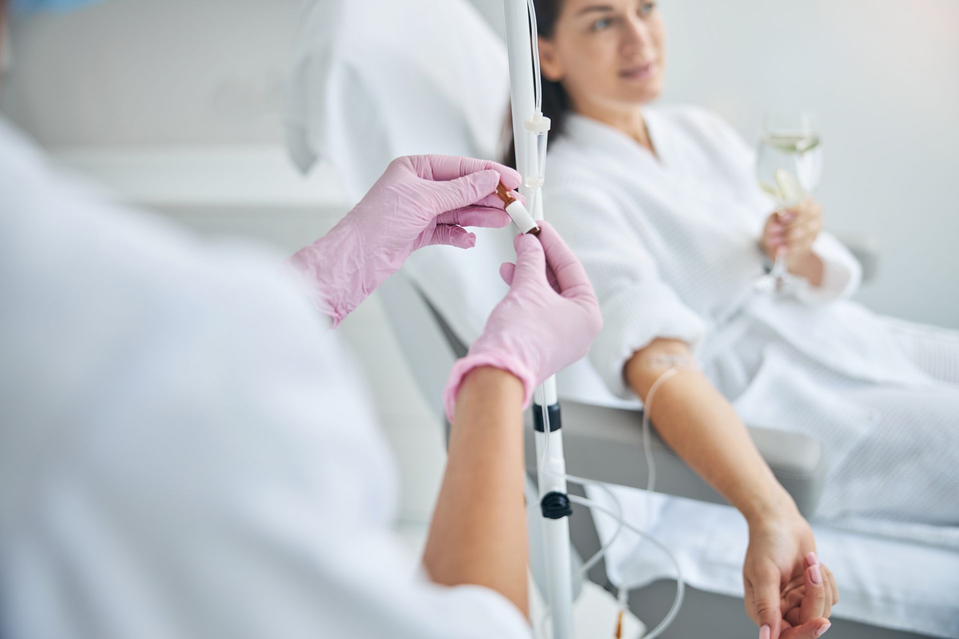 A woman is getting an iv in her arm while holding a glass of wine.