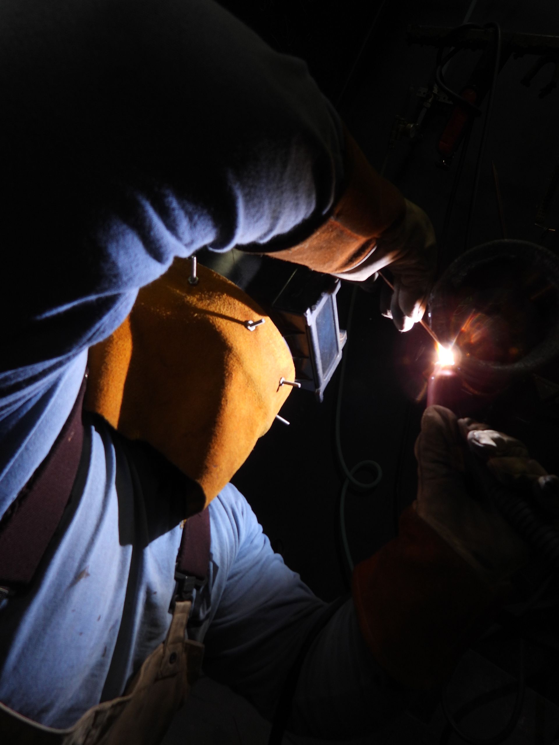 A man is welding a piece of metal in the dark