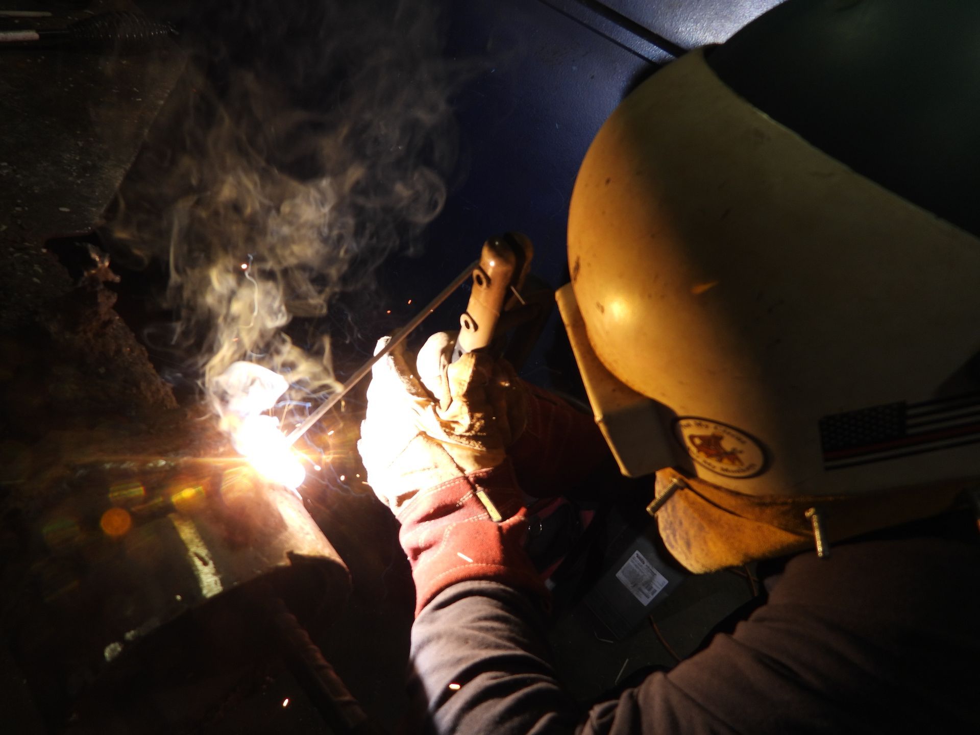 A man wearing a welding helmet is welding a piece of metal
