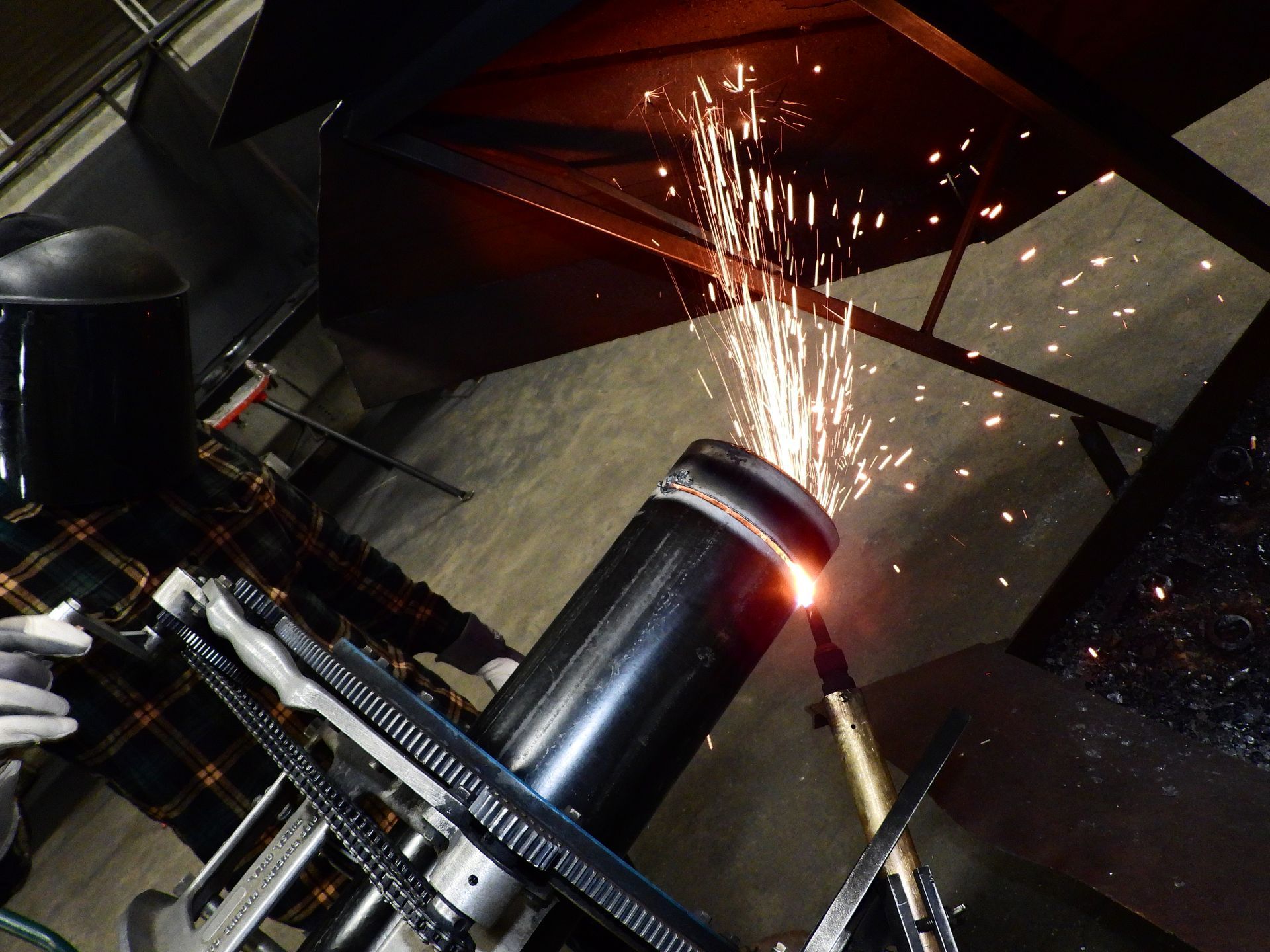 A man wearing a welding helmet is cutting a piece of metal