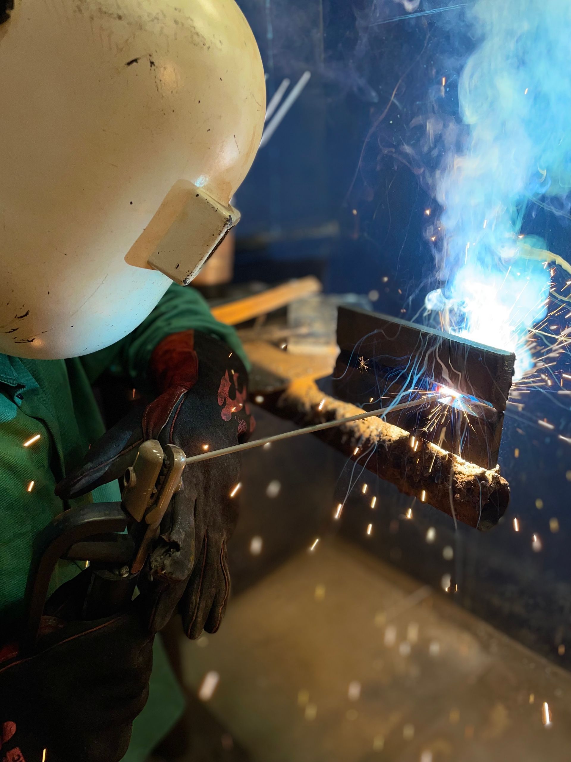 A man wearing a welding helmet is welding a piece of metal
