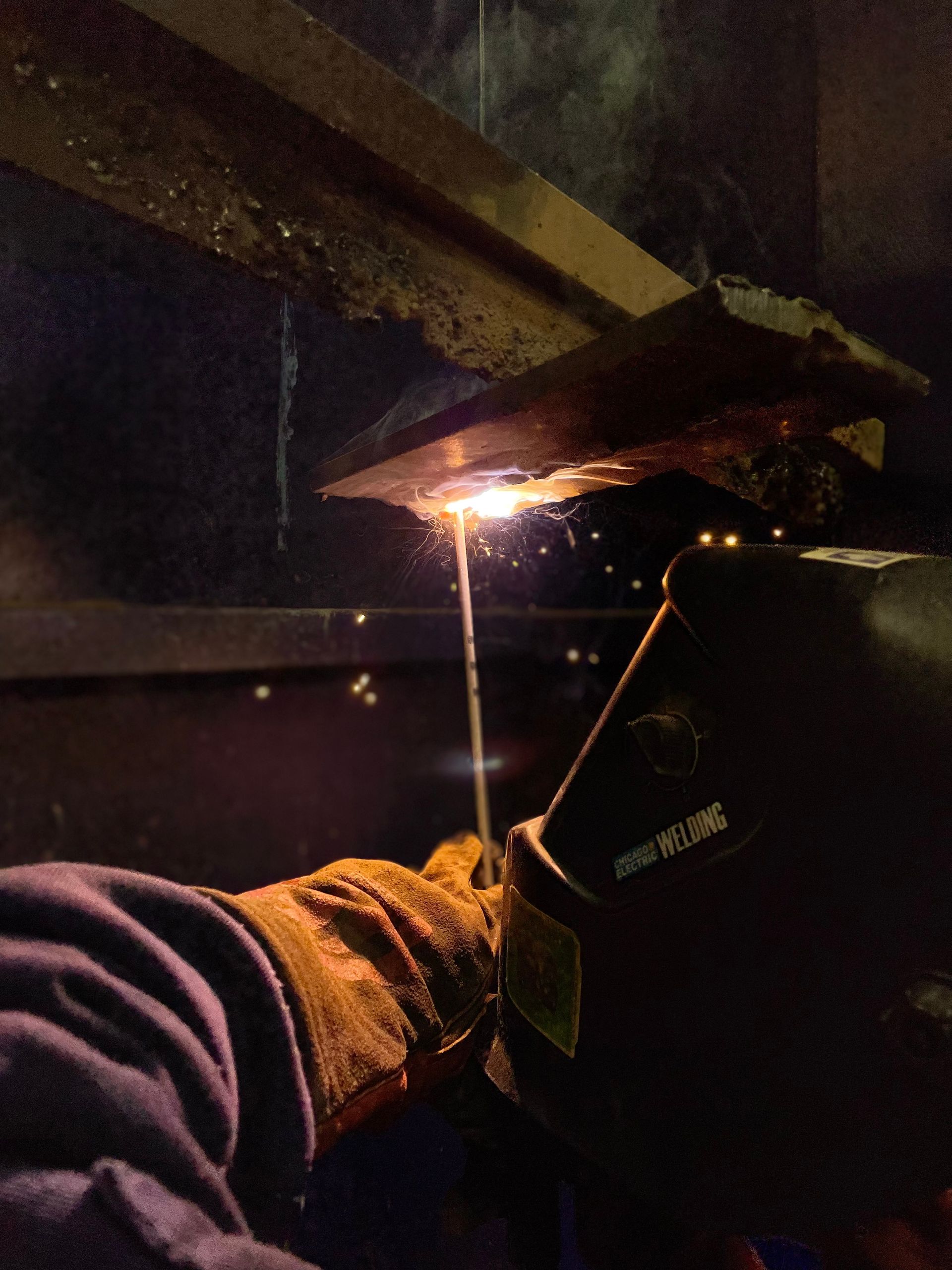 A person wearing a welding glove is welding a piece of metal