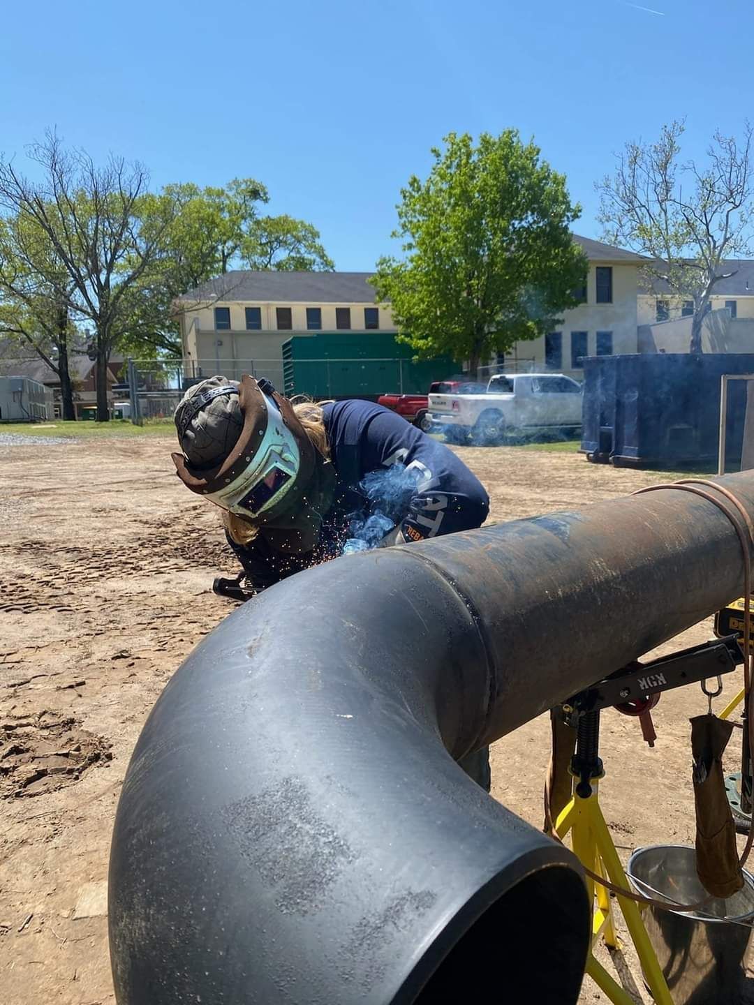A man is welding a pipe in a field.