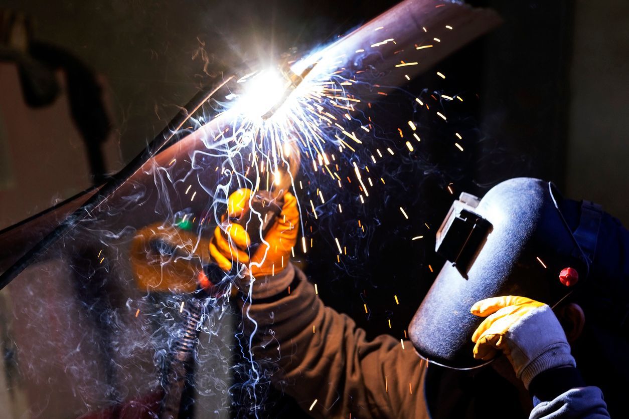 A man wearing a welding mask is welding a piece of metal.