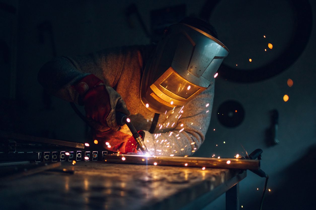 A man is welding a piece of metal in a dark room.