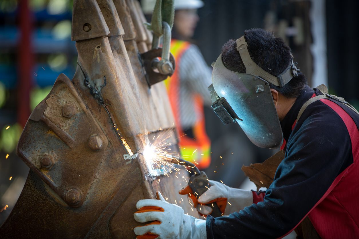 A man wearing a welding mask is welding a piece of metal.
