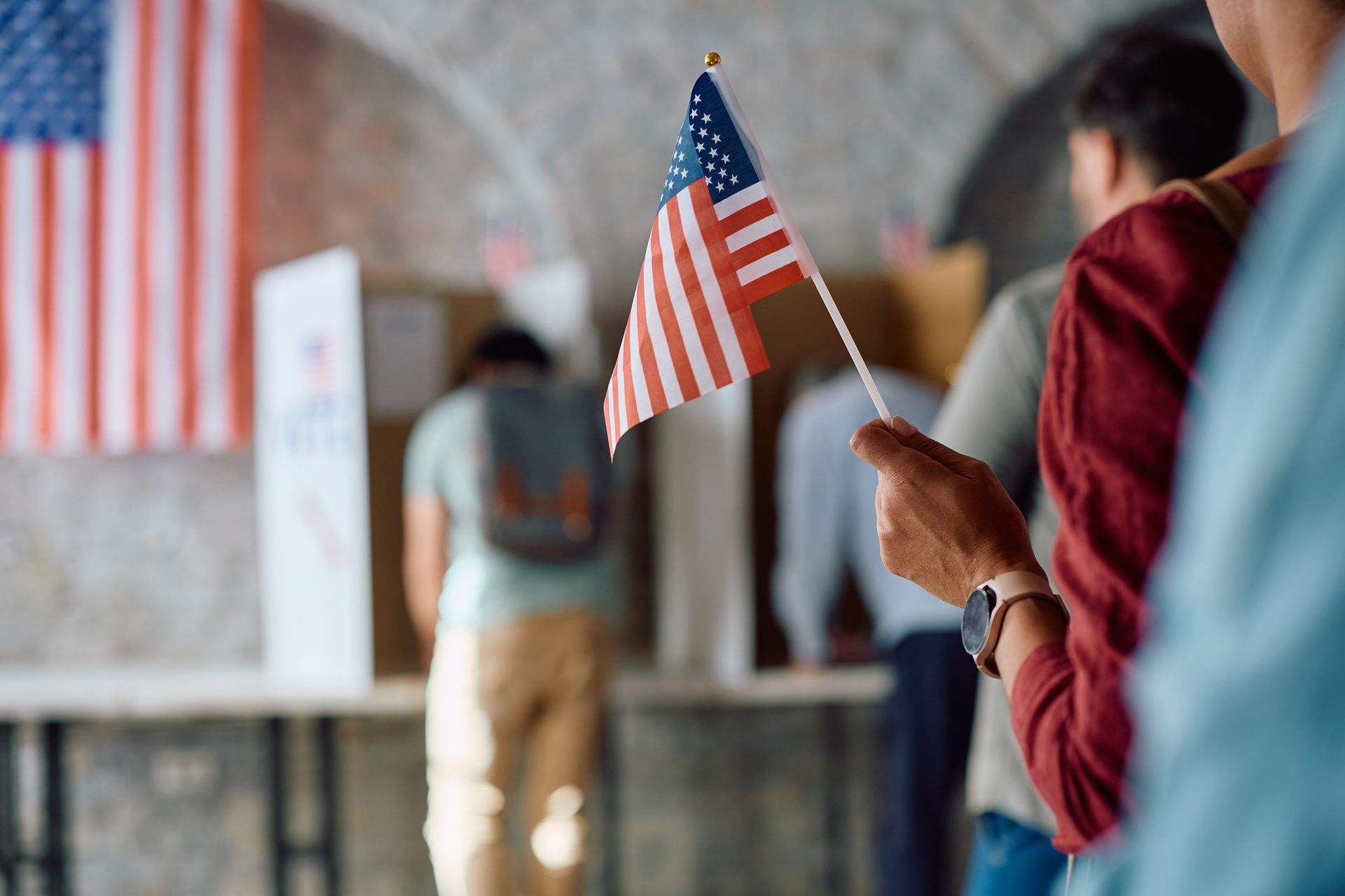 A person is holding an american flag in a voting booth.