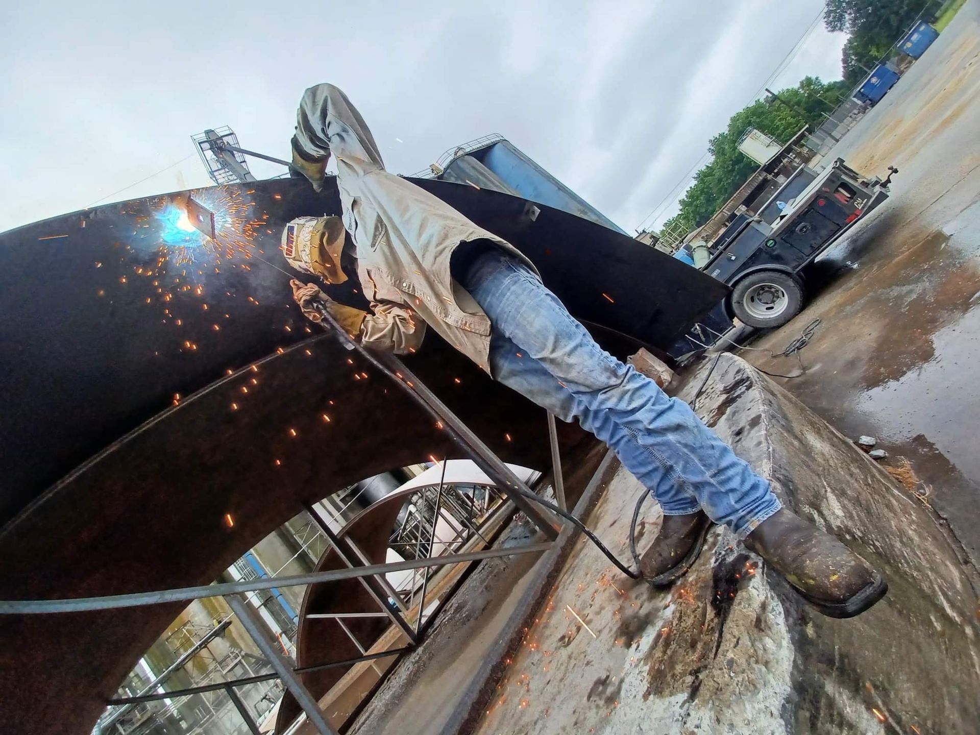 A man is welding a piece of metal in a parking lot