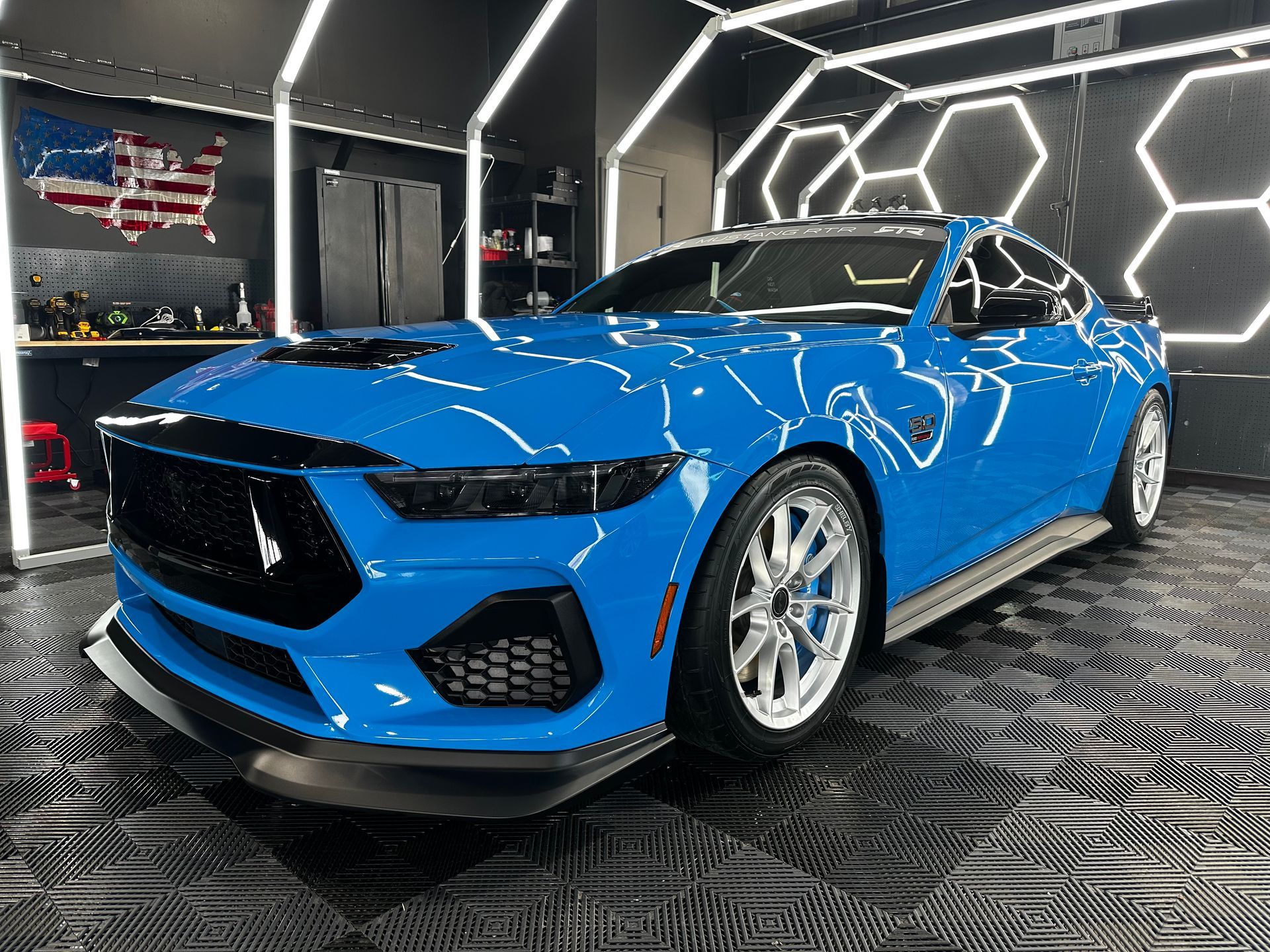 A black harley davidson motorcycle is parked in a garage next to a blue corvette.