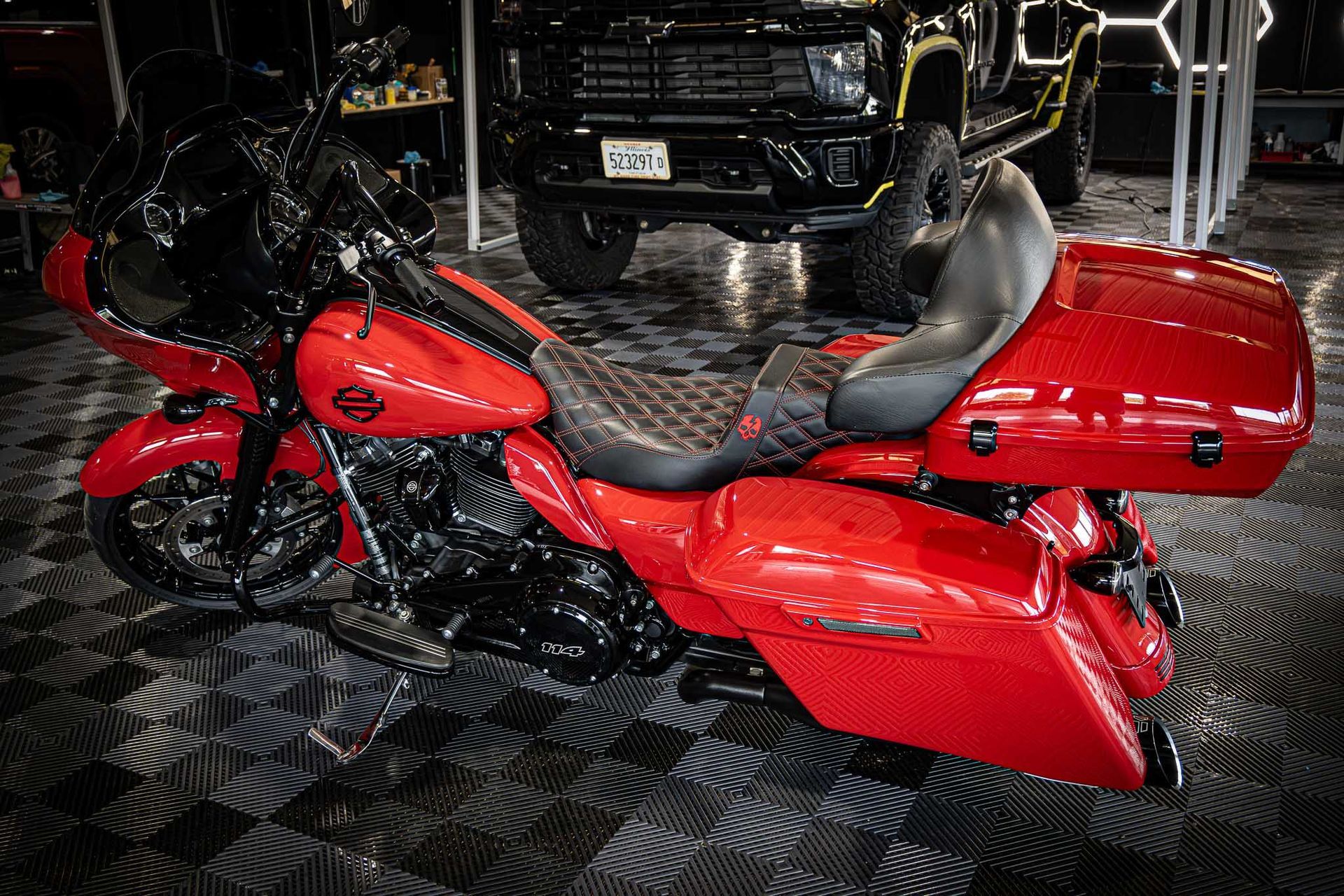 A red harley davidson motorcycle is parked in a garage next to a black truck.