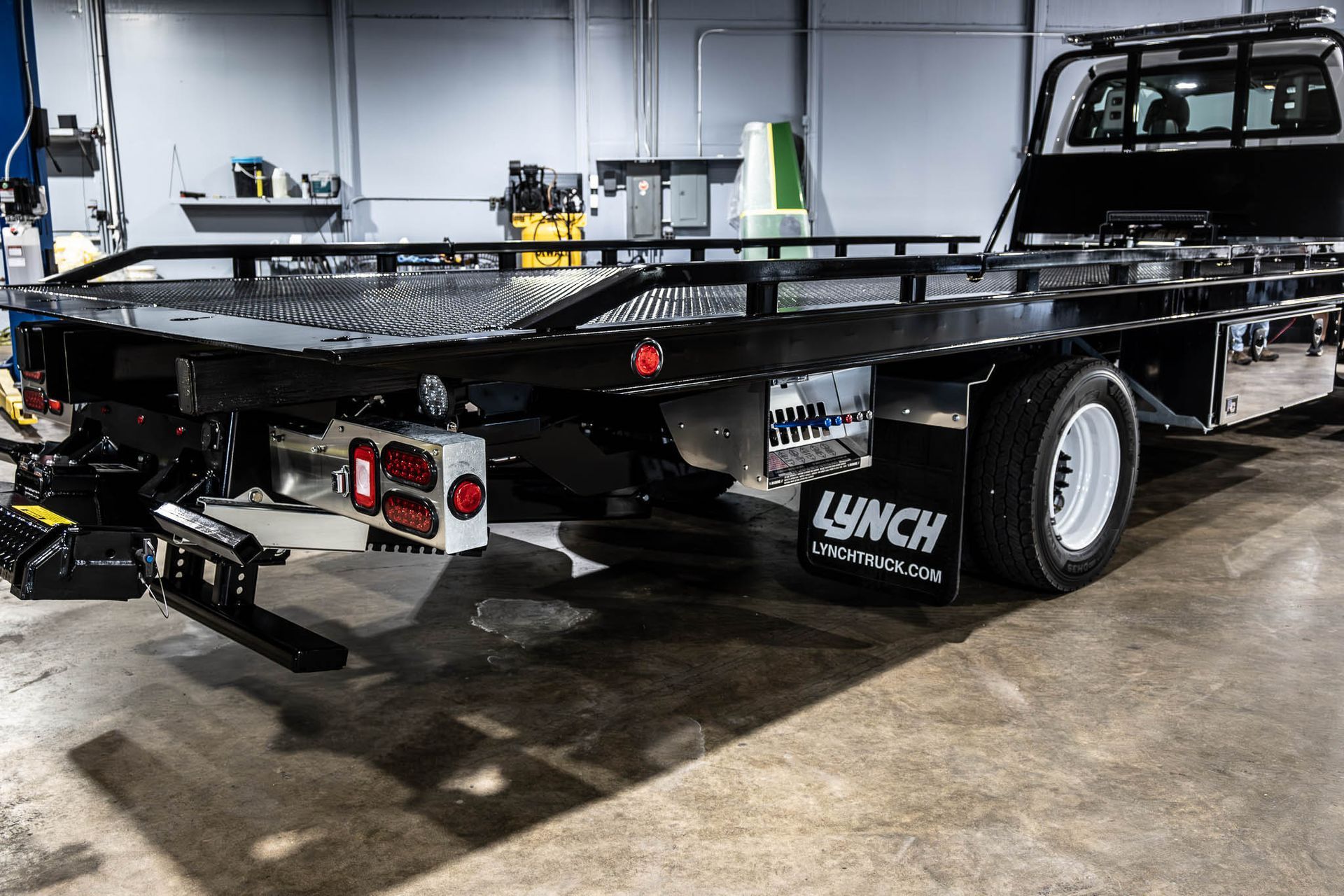 A tow truck with a flat bed is parked in a garage.