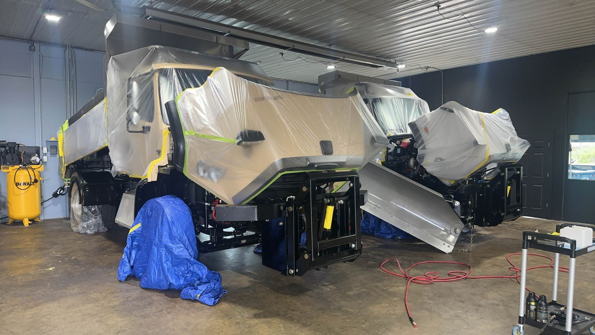 A large vehicle is sitting in a garage covered in plastic.