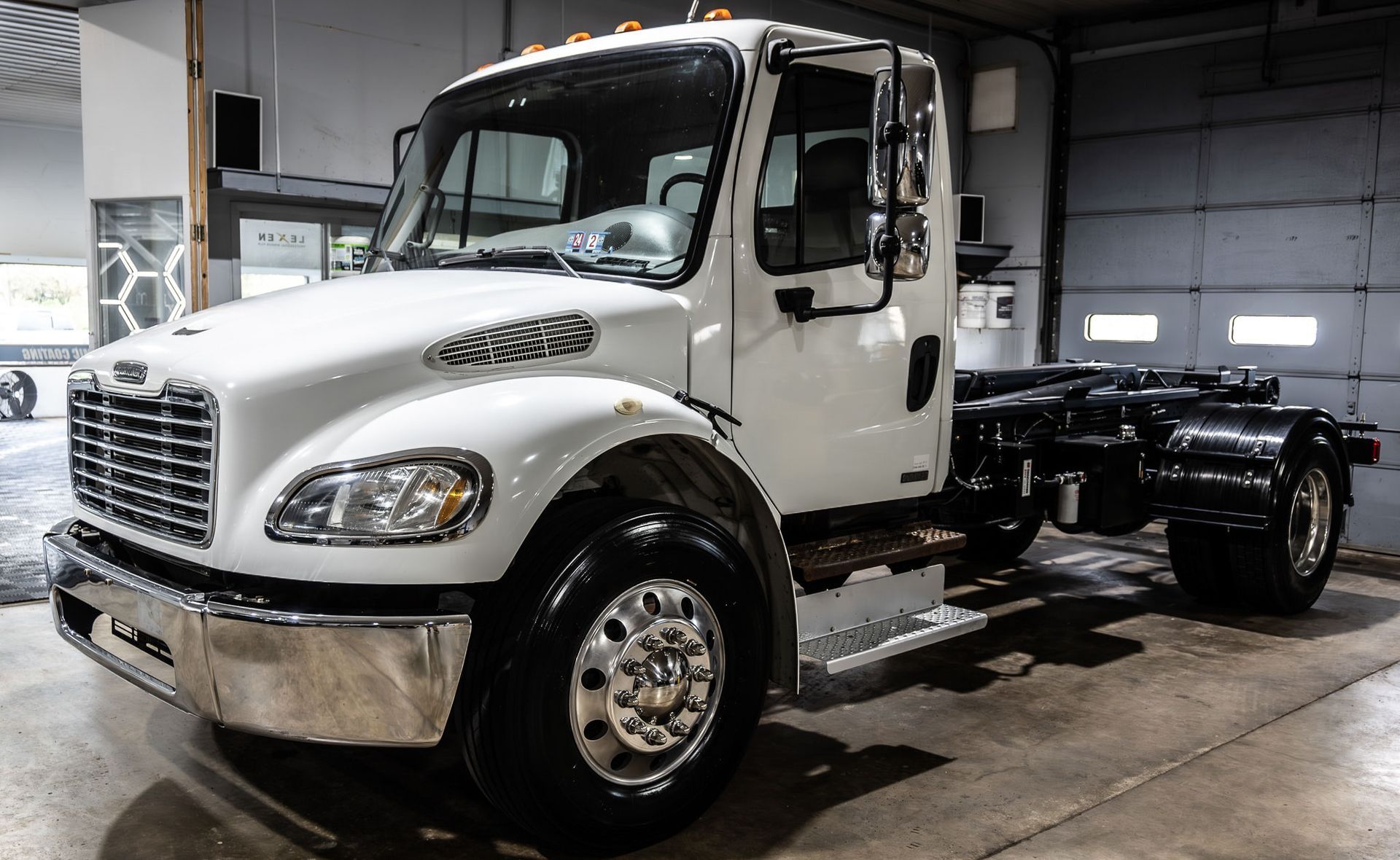 A white truck is parked in a garage next to a garage door.