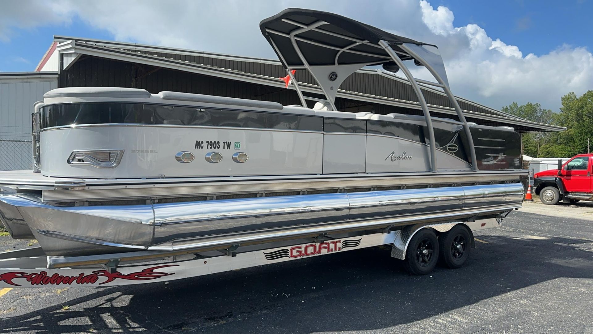 A silver pontoon boat is parked on a trailer in front of a building.