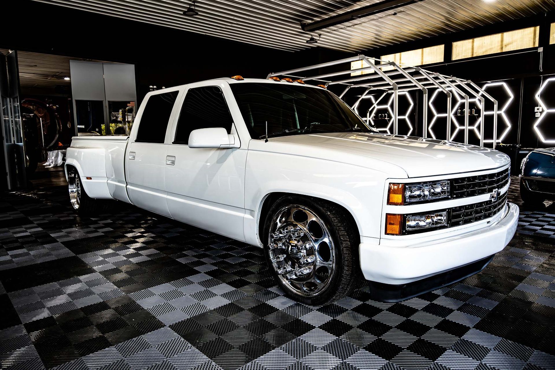 A white truck is parked on a checkered floor in a garage.