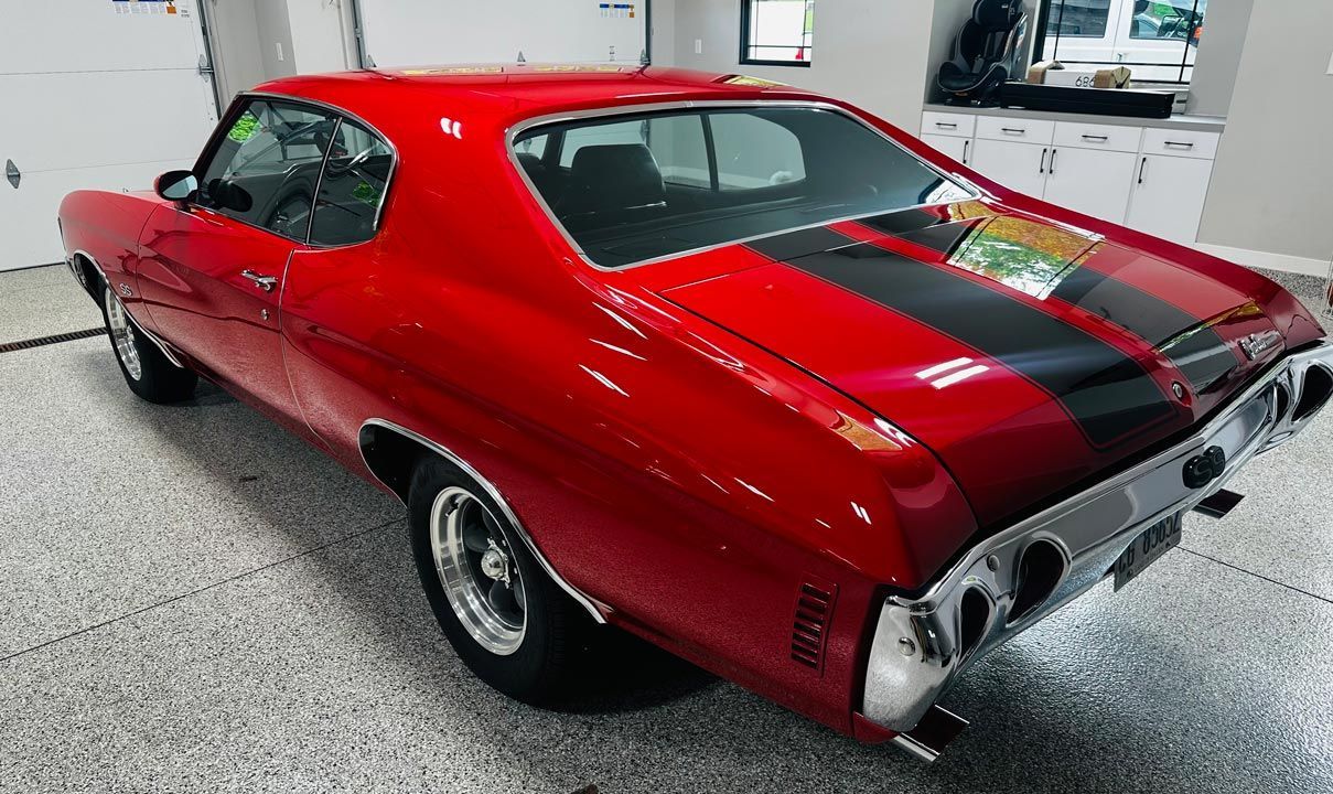 A red muscle car is parked in a garage.