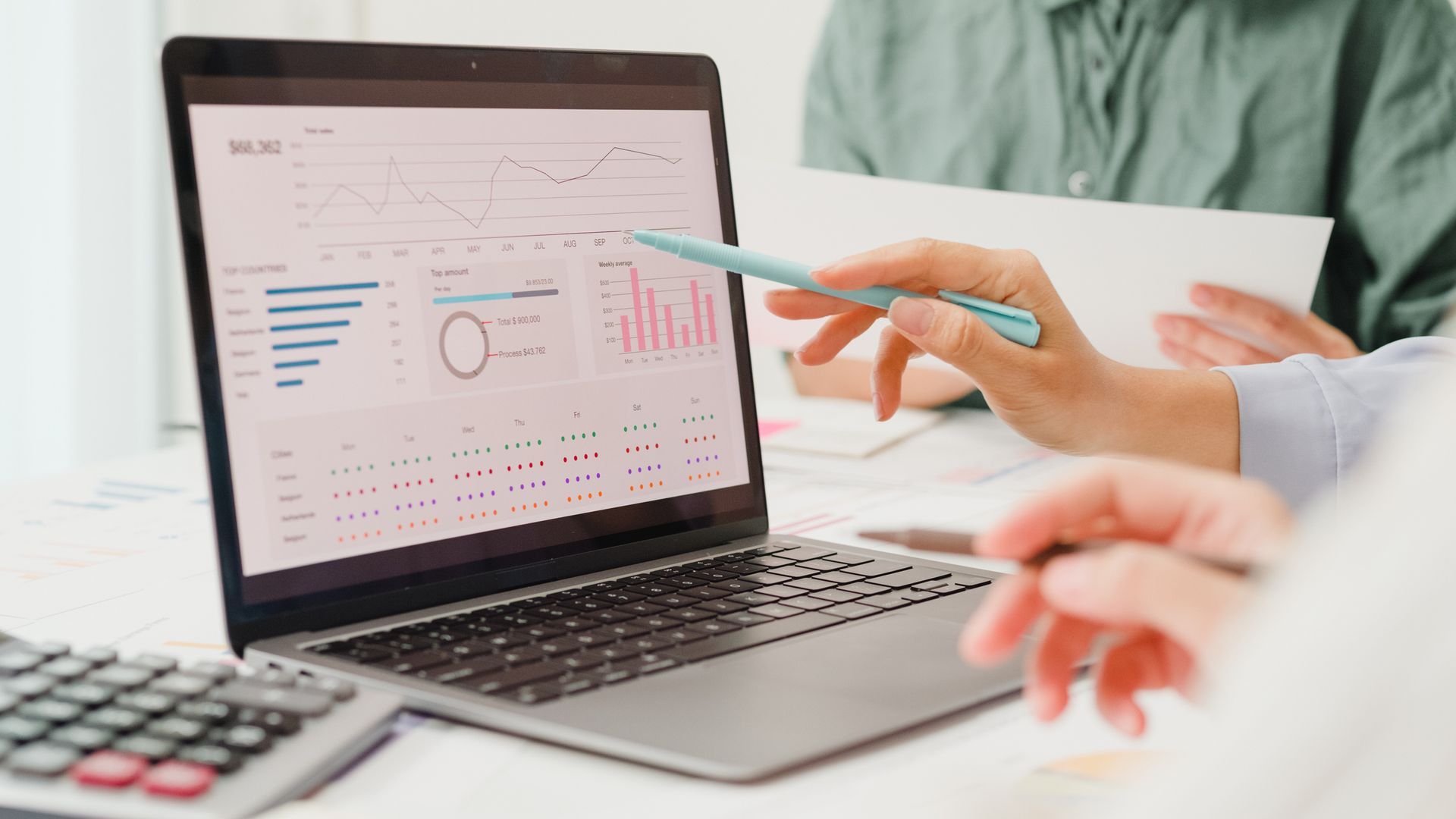 People analyzing financial data on a laptop screen, using a pen to point at charts.