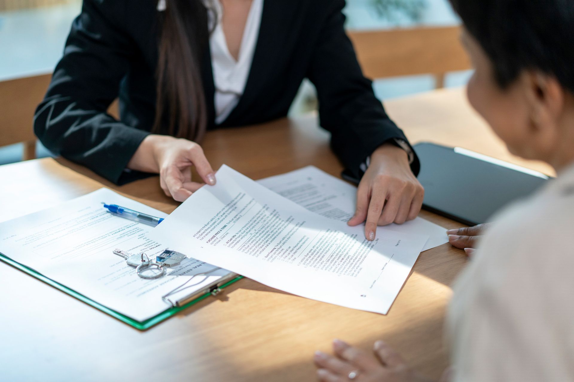 Woman in suit pointing at a document, explaining it to another woman at a table.