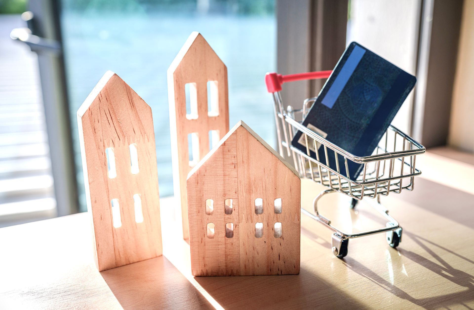 Wooden house models with a shopping cart holding a credit card.