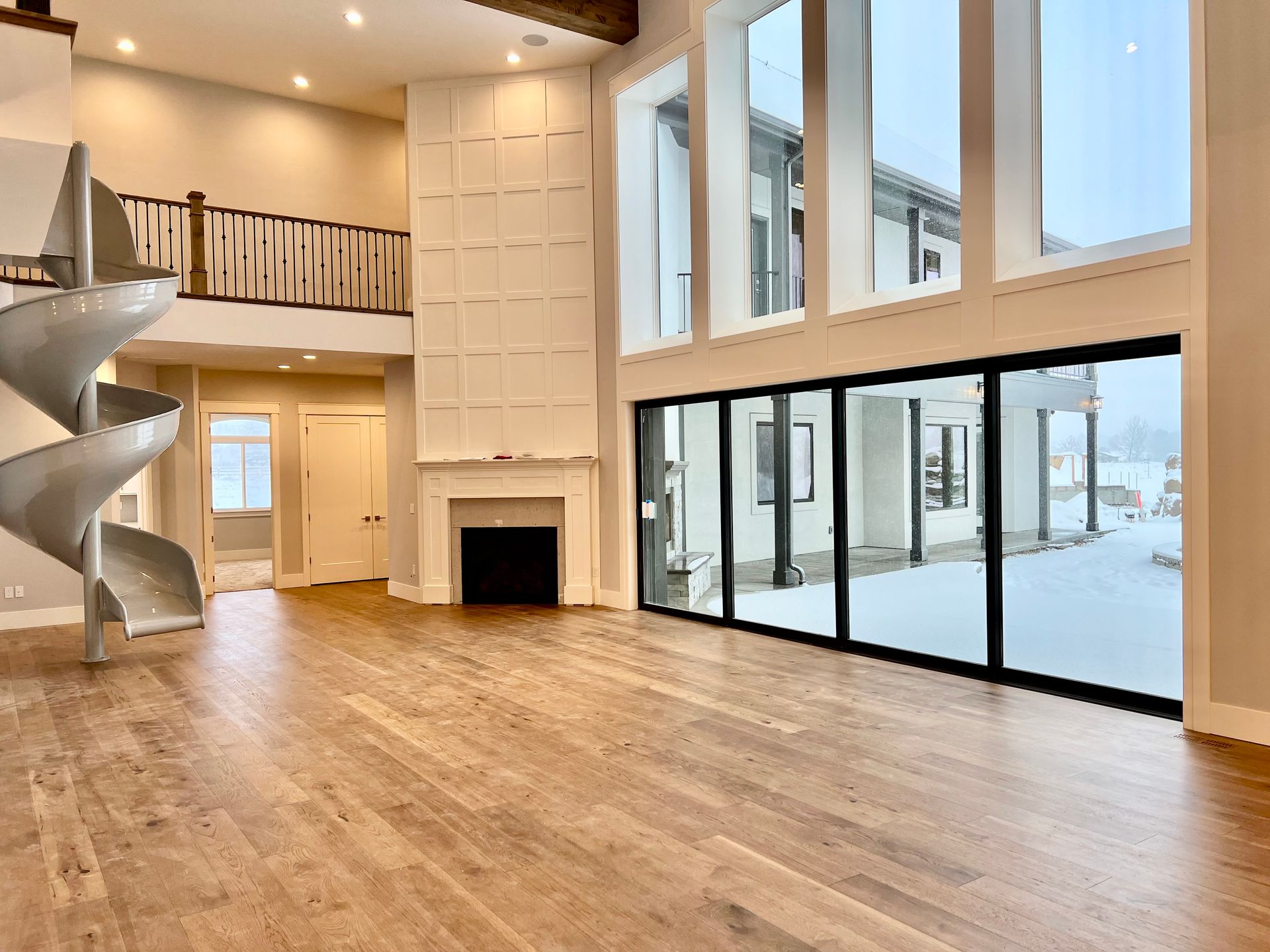 Bright open living room with hardwood floors, loft railing, fireplace, spiral staircase, and floor-to-ceiling windows