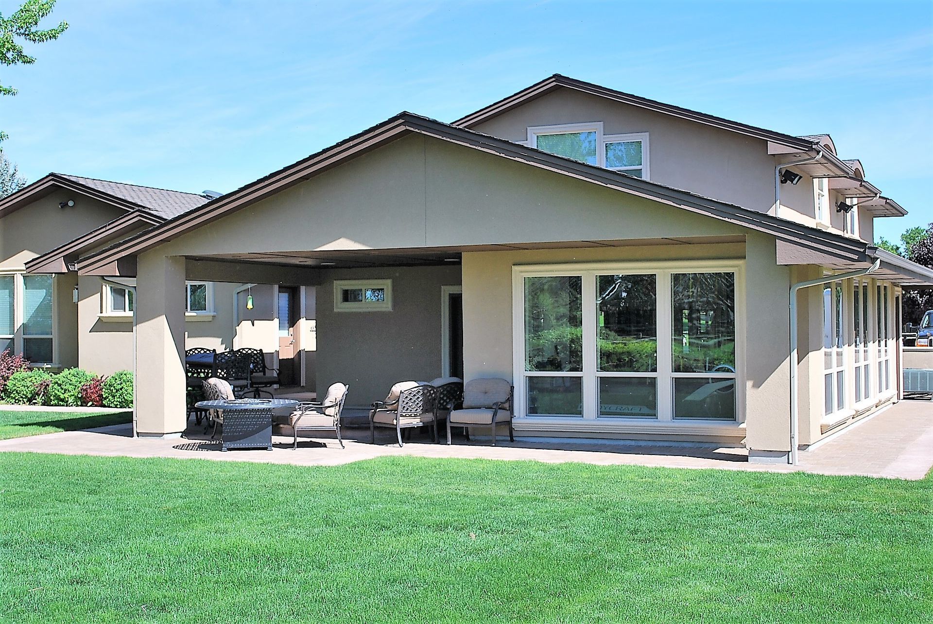 Single-story suburban house with a patio, large windows, and a green lawn