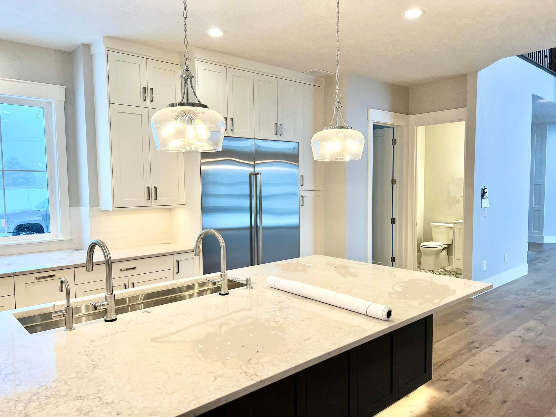 Modern white kitchen with marble island, stainless fridge, pendant lights, and wood floors