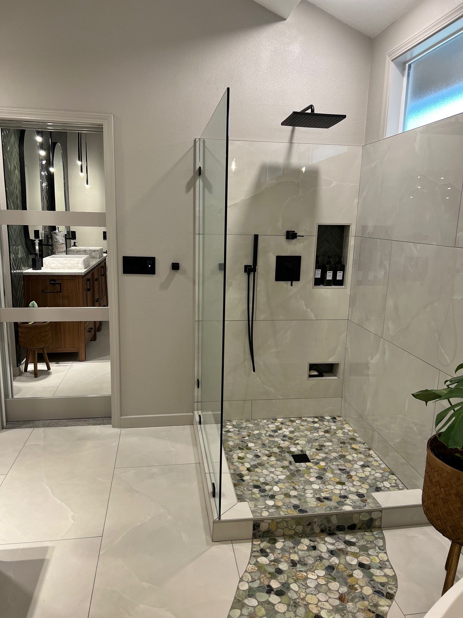 Modern bathroom with a glass shower, pebble shower floor, and large mirror on the left.