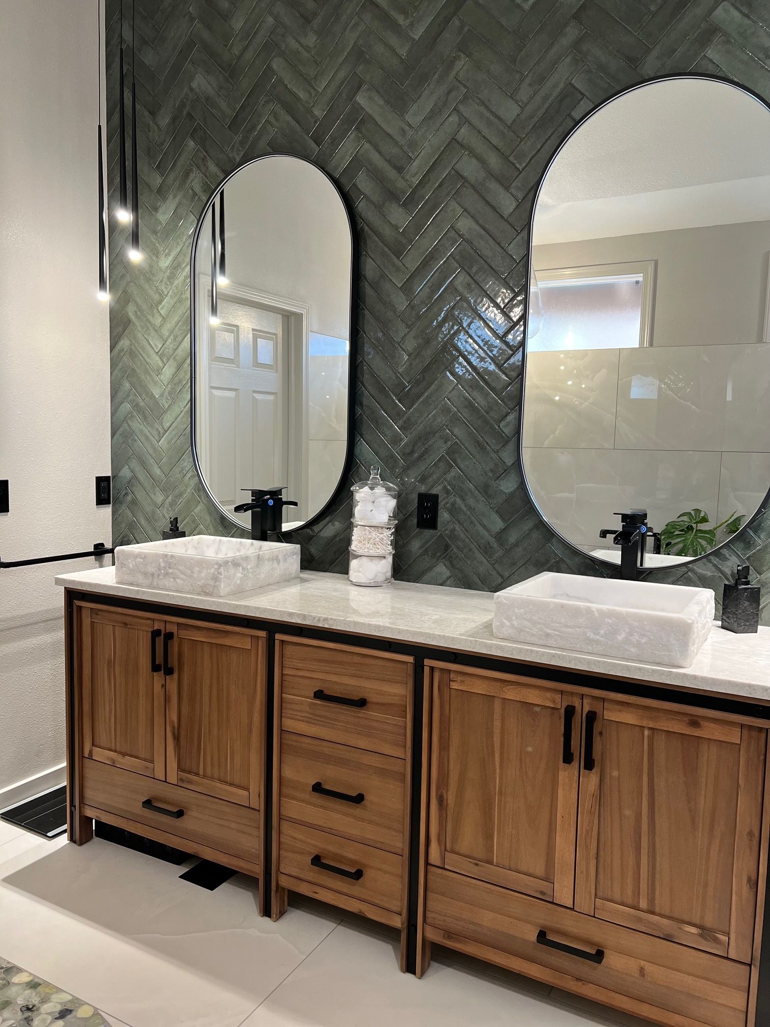 Modern bathroom vanity with wood cabinets, double sinks, and a large round black-framed mirror without a person.