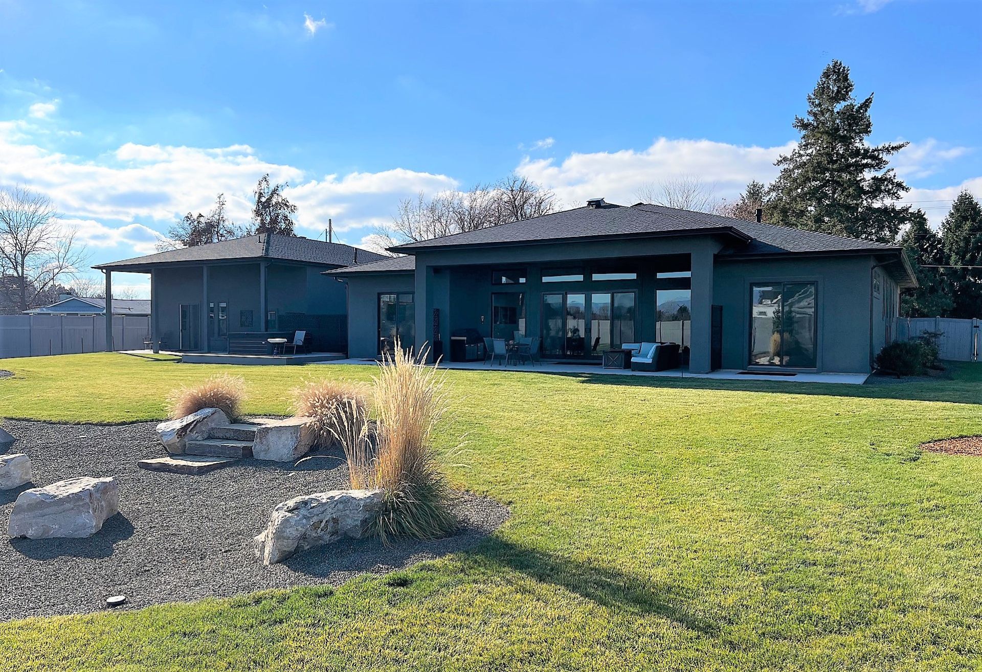 Modern single-story house with large windows, a grassy yard, and a rock garden under a blue sky
