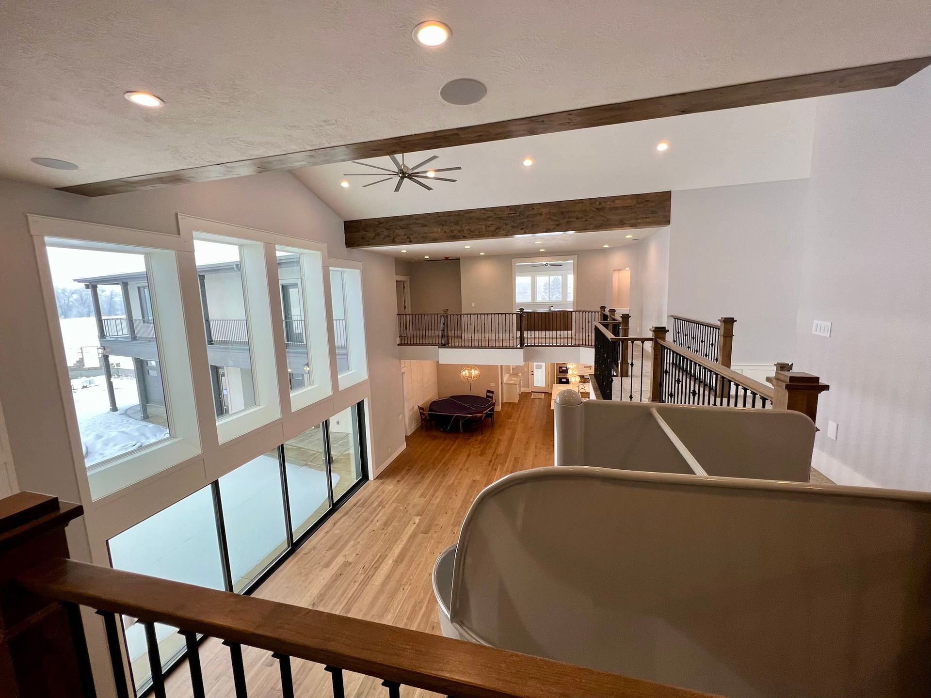 Modern open interior with wood floors, white walls, large windows, and a loft railing overlooking a stairway