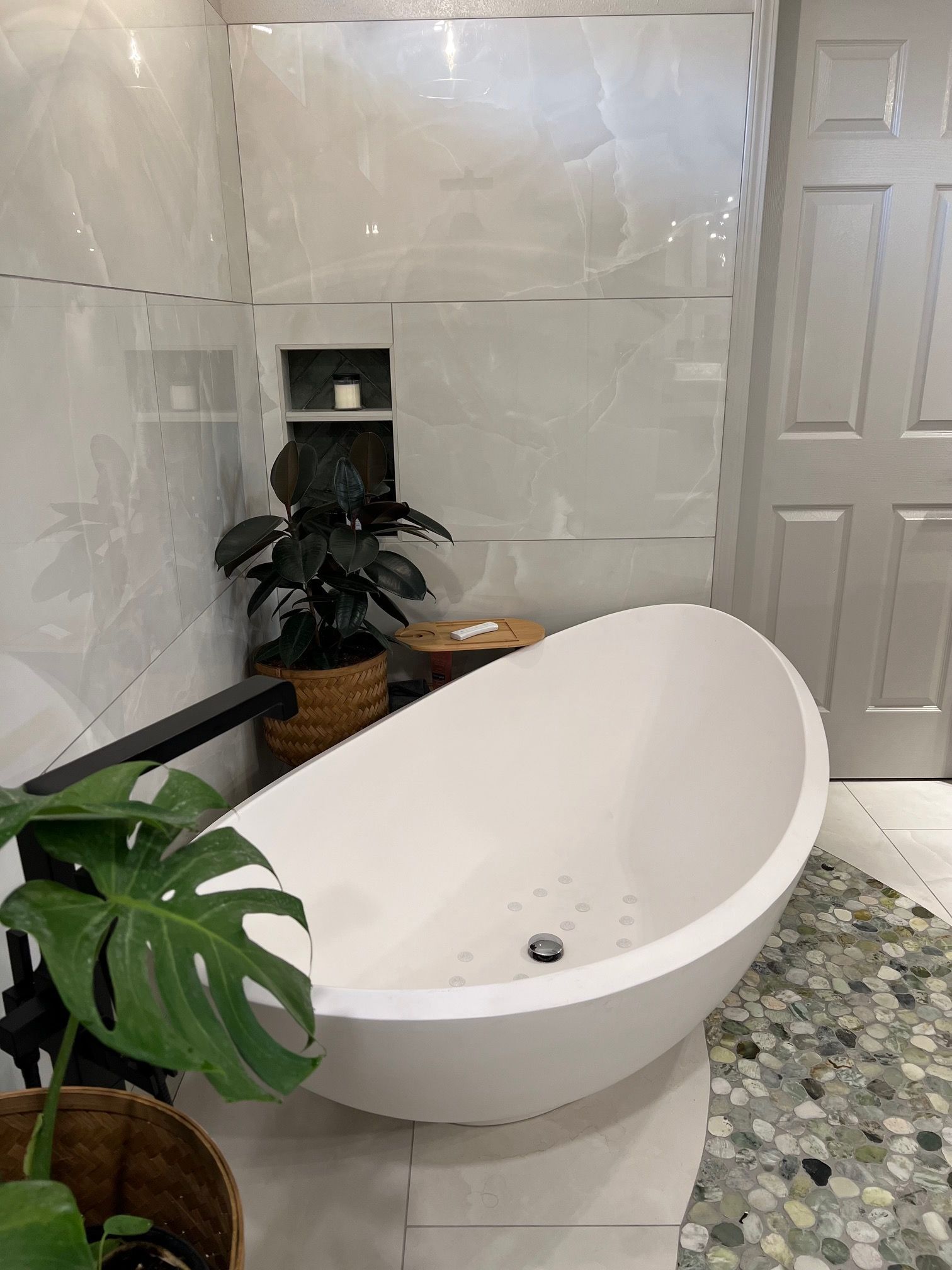 Modern bathroom with a white oval freestanding tub, tiled walls, and potted plants.