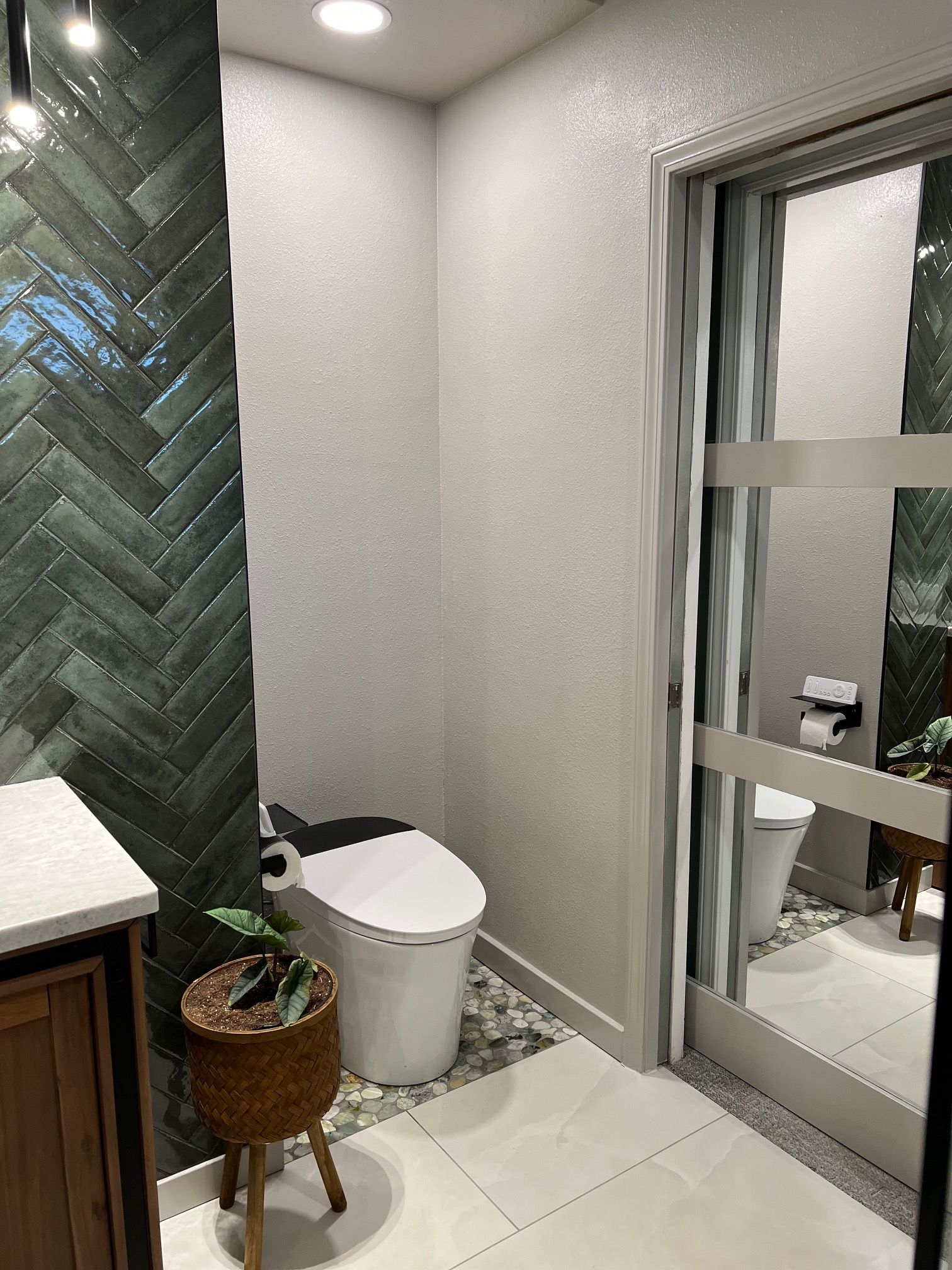 Small modern bathroom with toilet, herringbone green tile wall, sink, and glass shower door