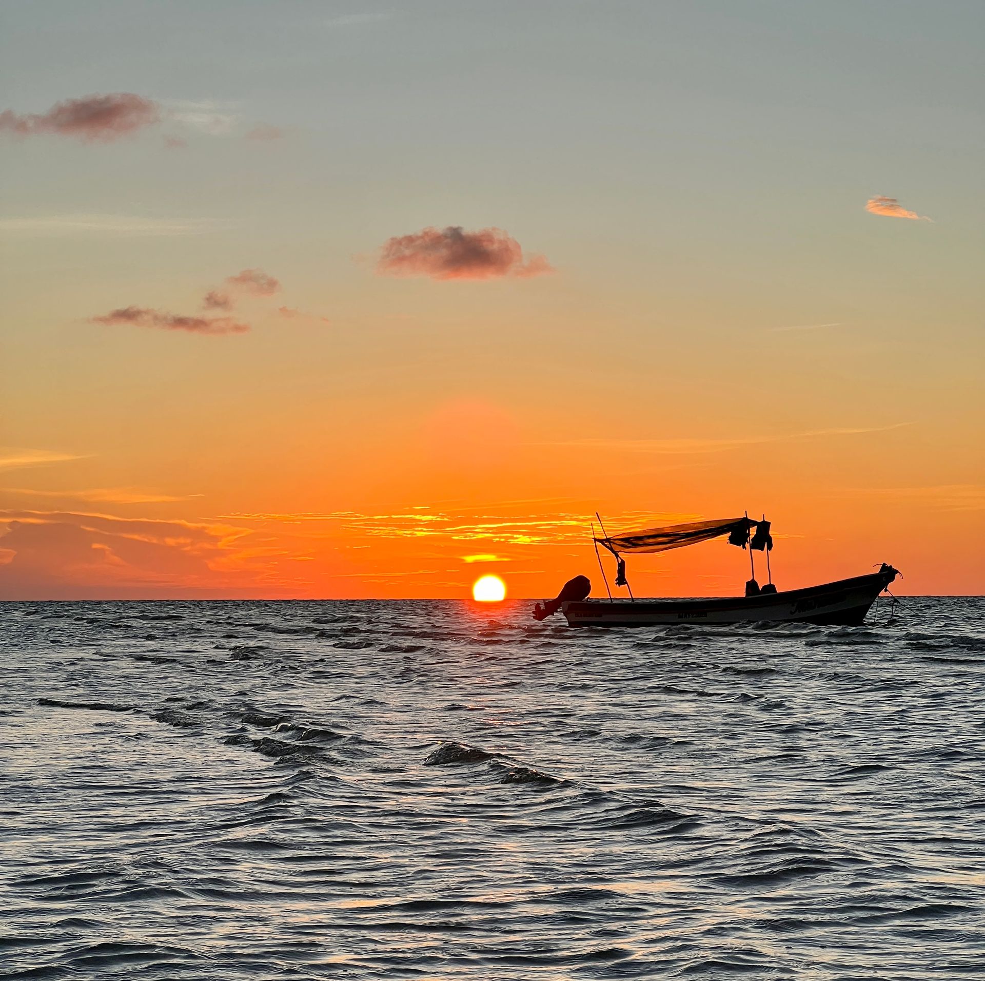 Silueta de barco contra un atardecer naranja vibrante sobre el océano.