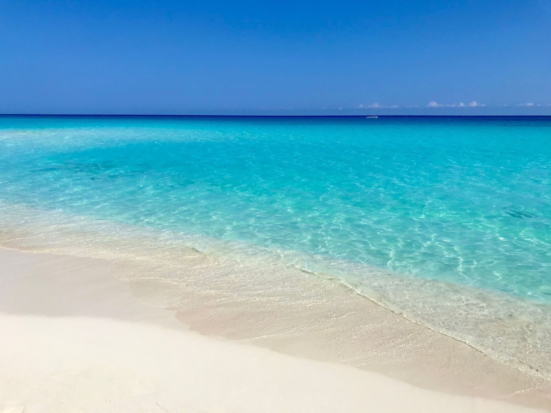 Un océano turquesa brillante se encuentra con una playa de arena blanca bajo un cielo azul claro.