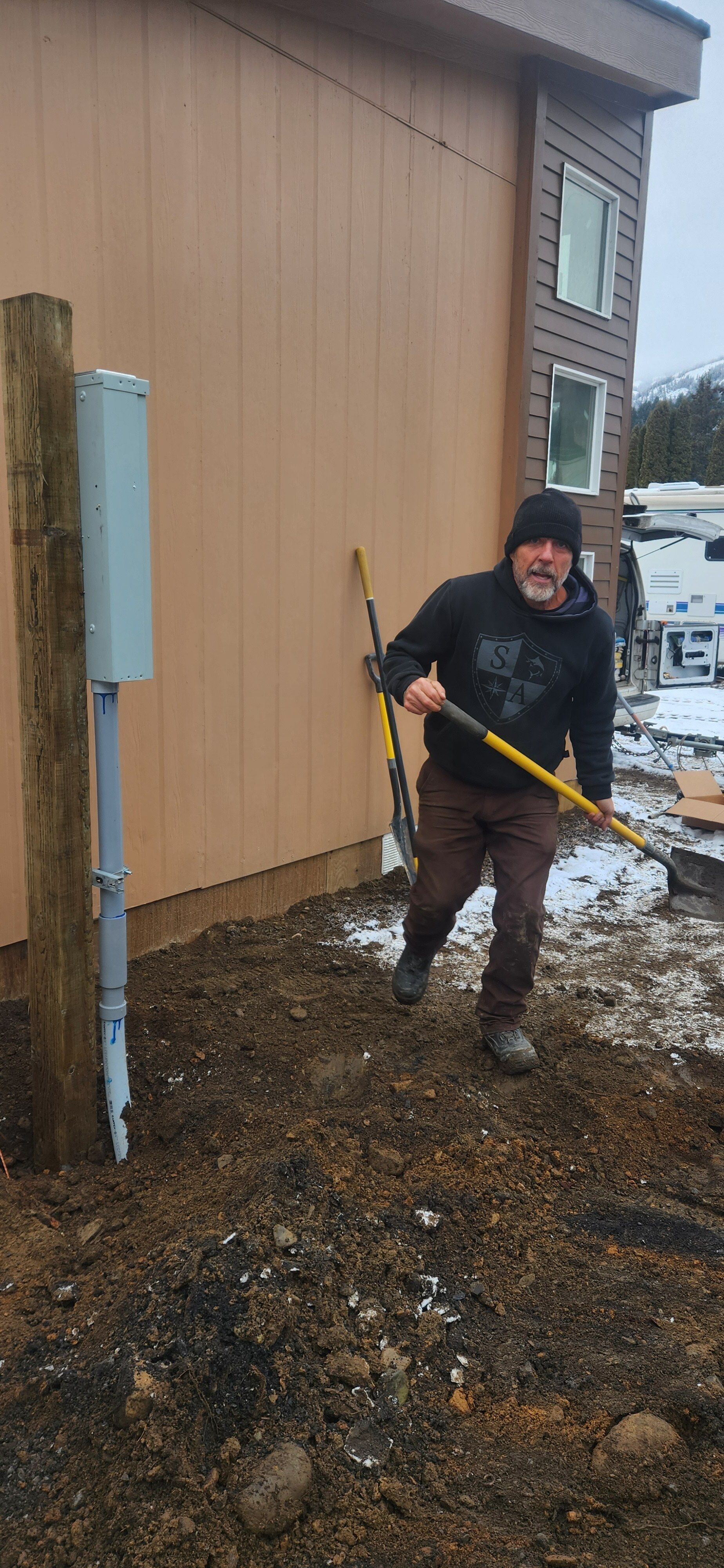 A man is digging in the dirt with a shovel in front of a house.