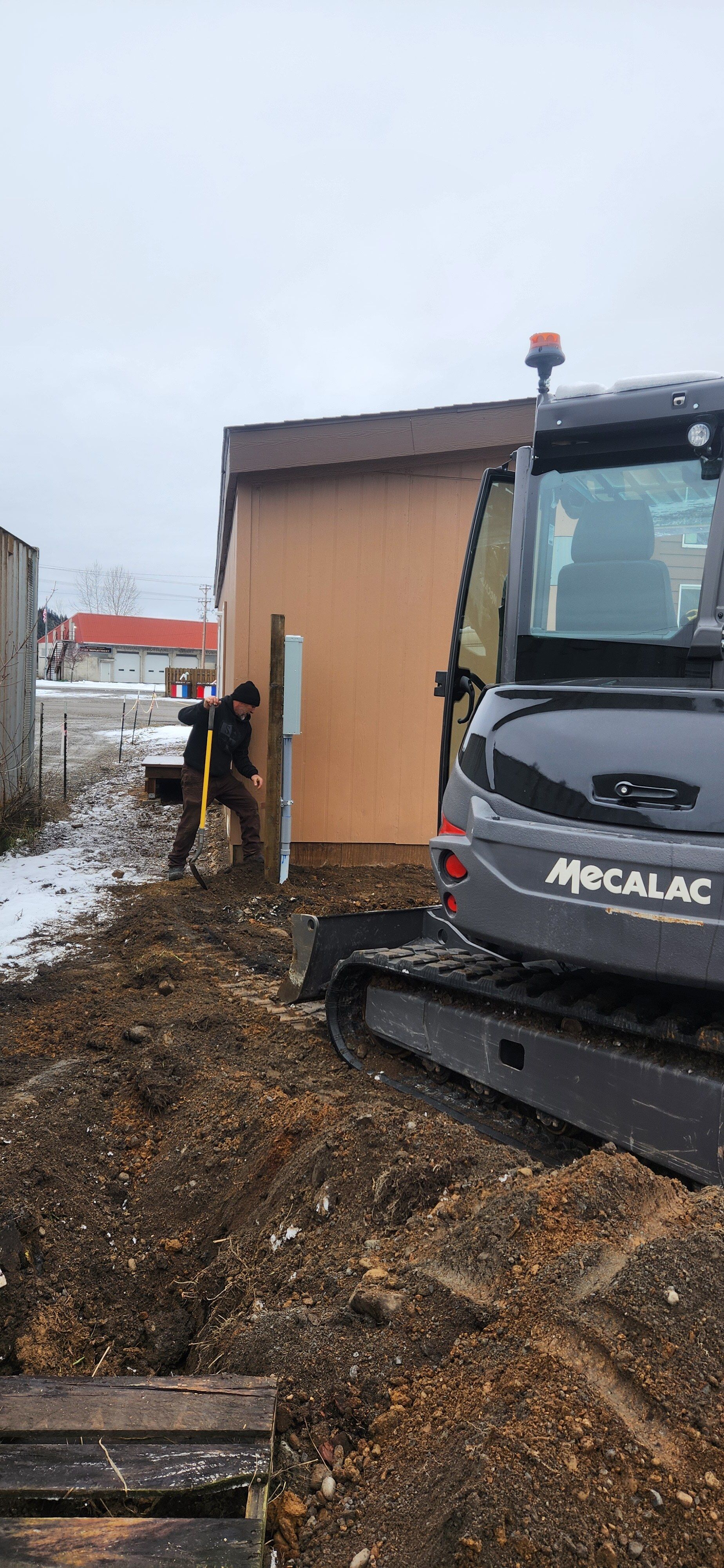 A man is digging in the dirt next to a large excavator.