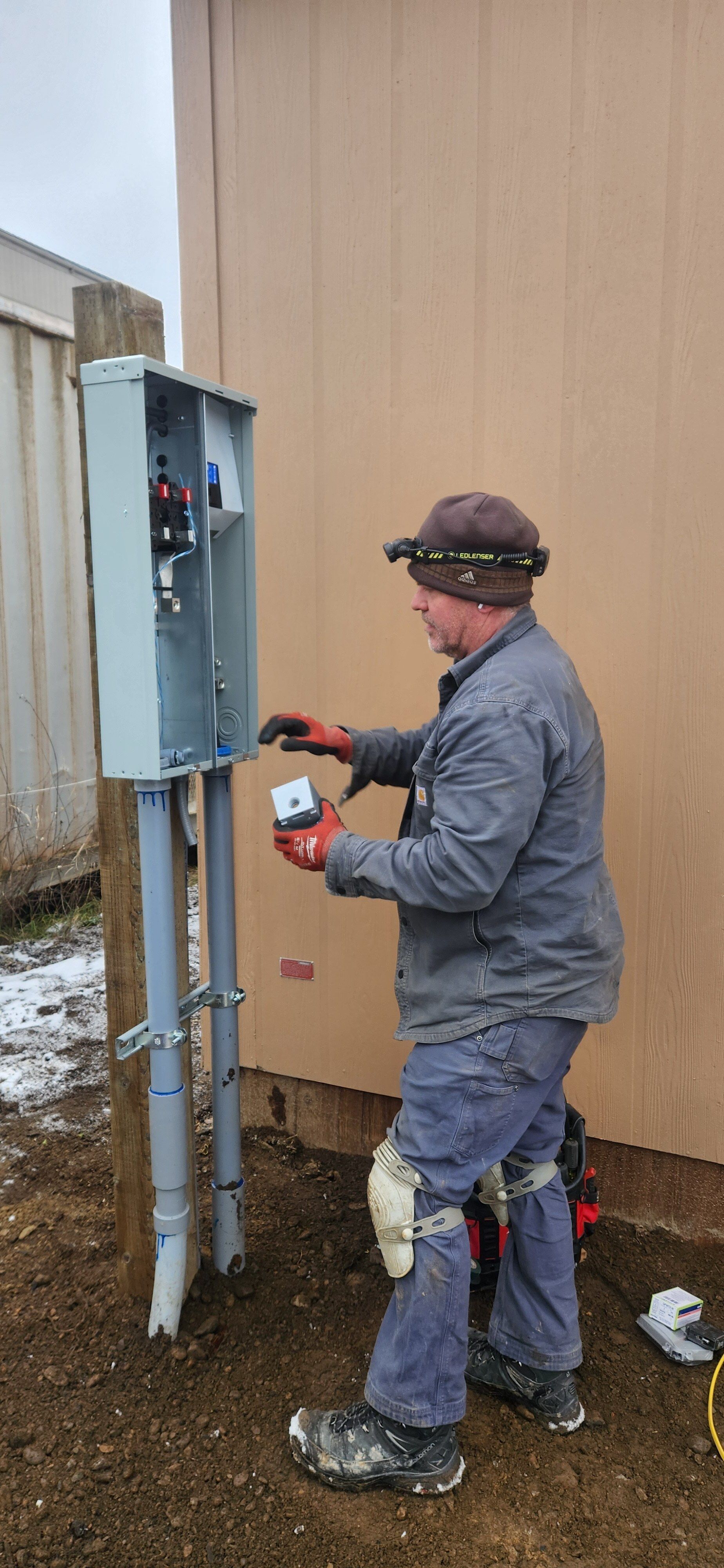 A man is working on an electrical box outside of a building.