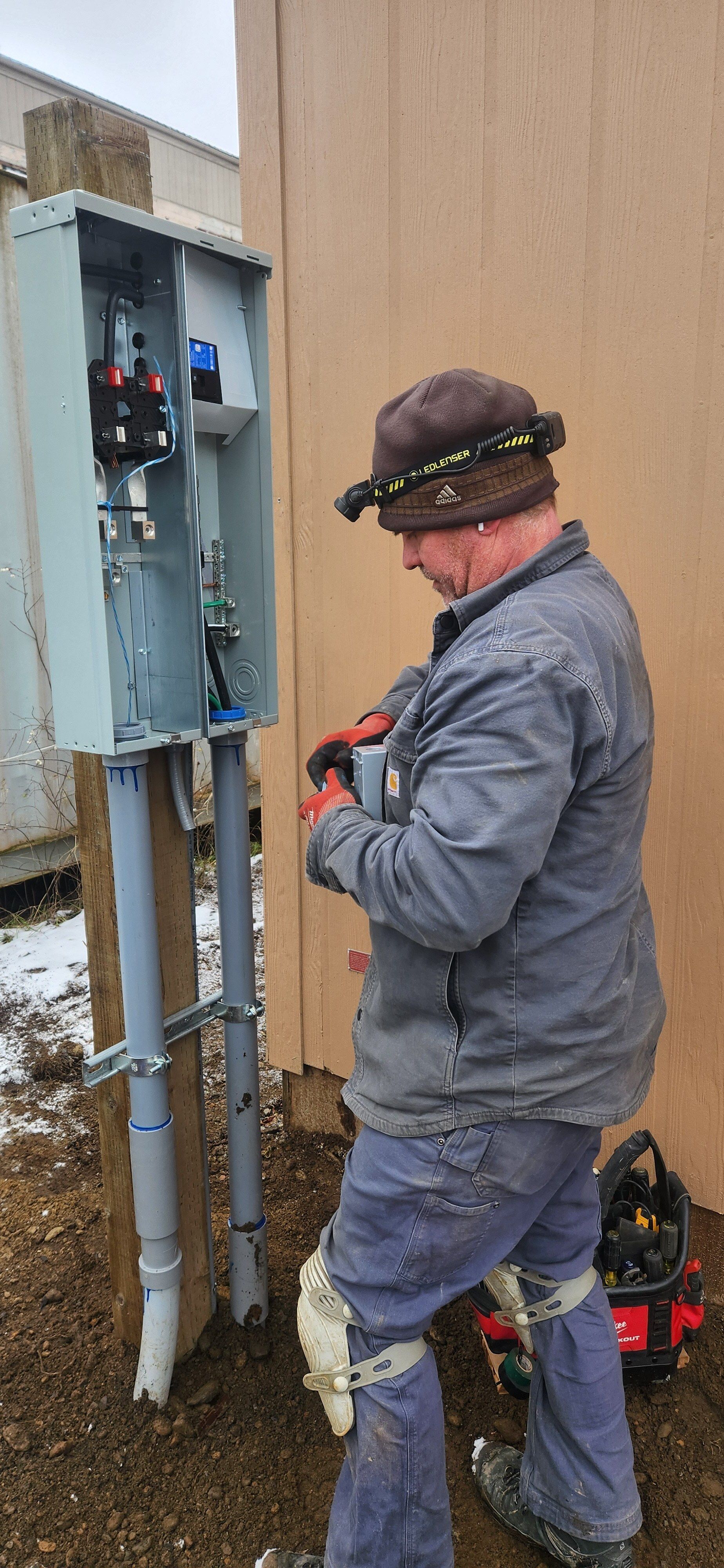 A man is working on an electric box outside of a building.