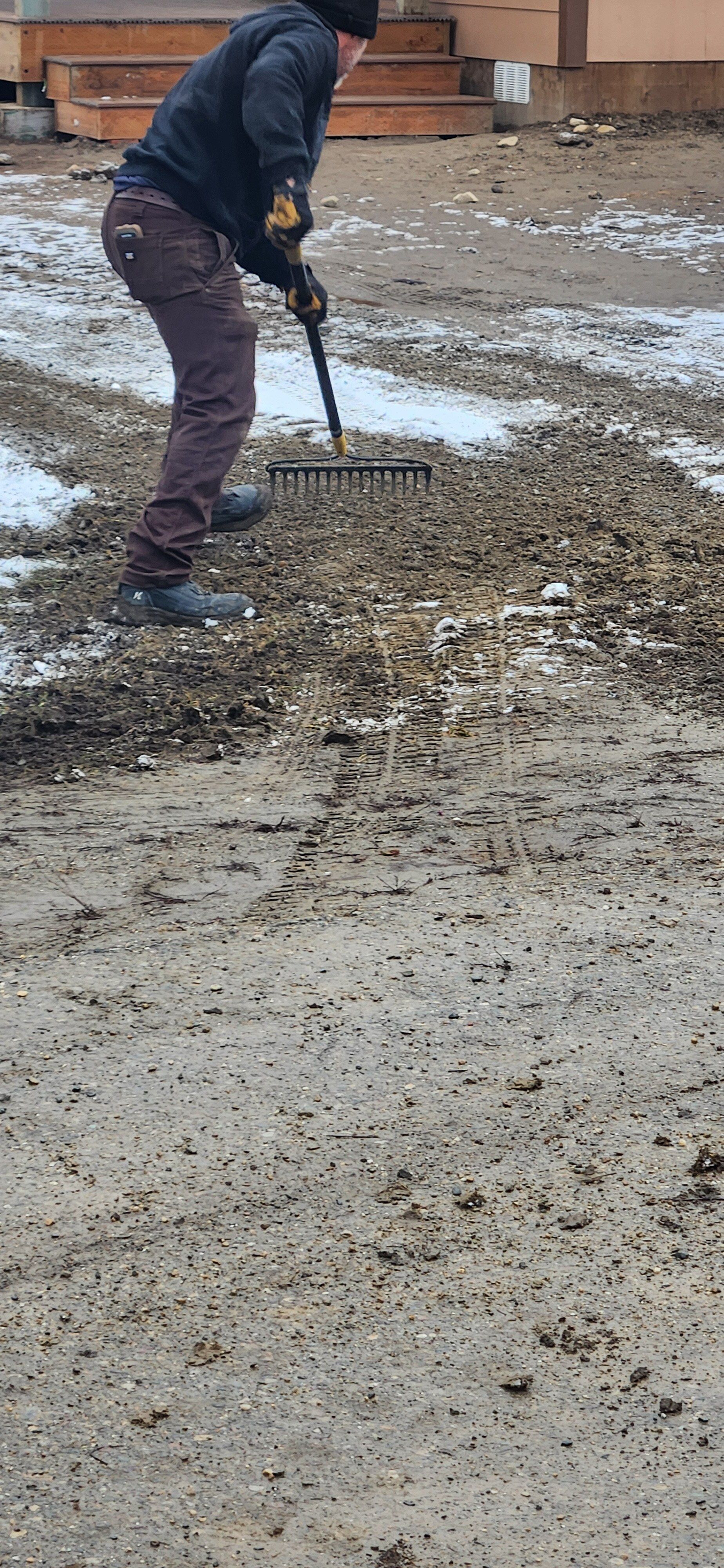 A man is raking dirt in a yard with a rake.