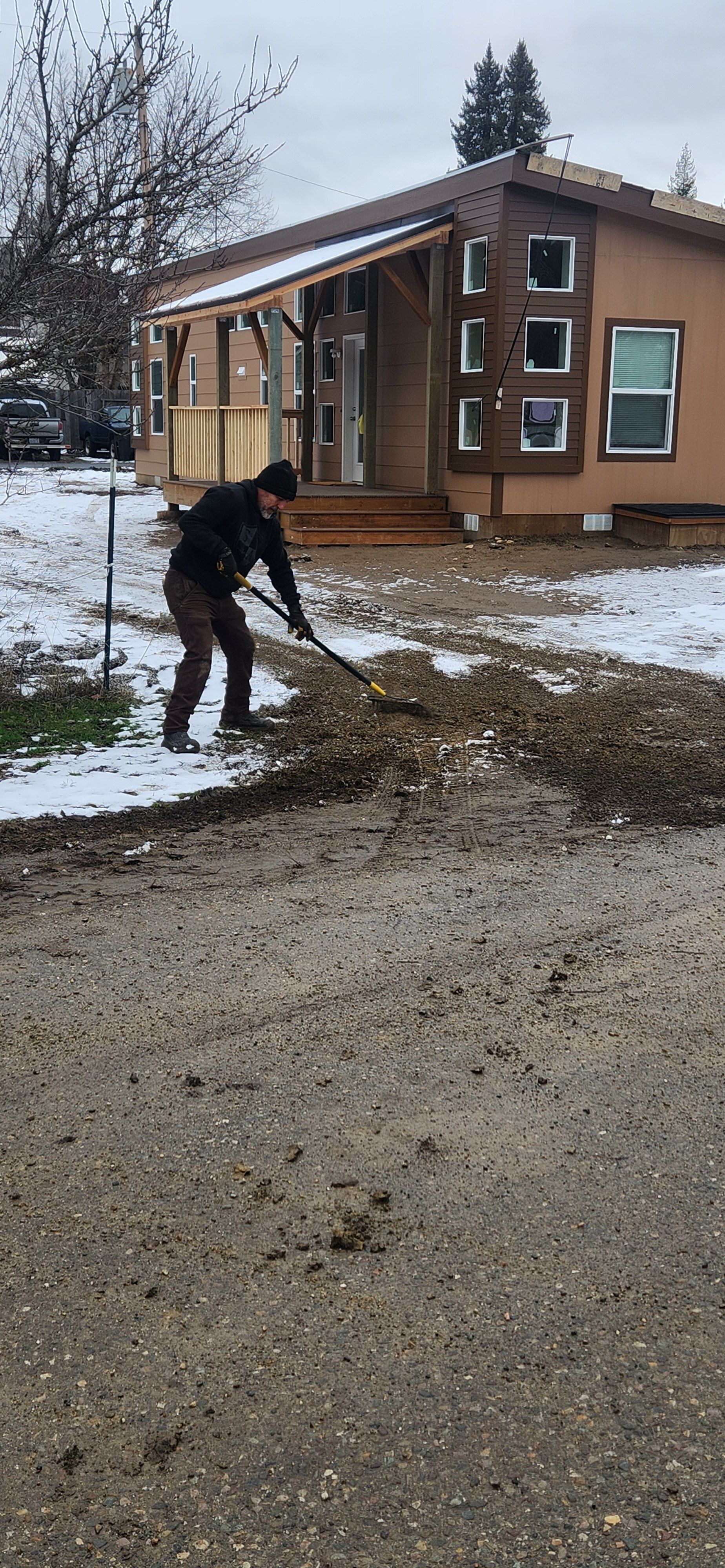 A man is raking snow from the ground in front of a house.