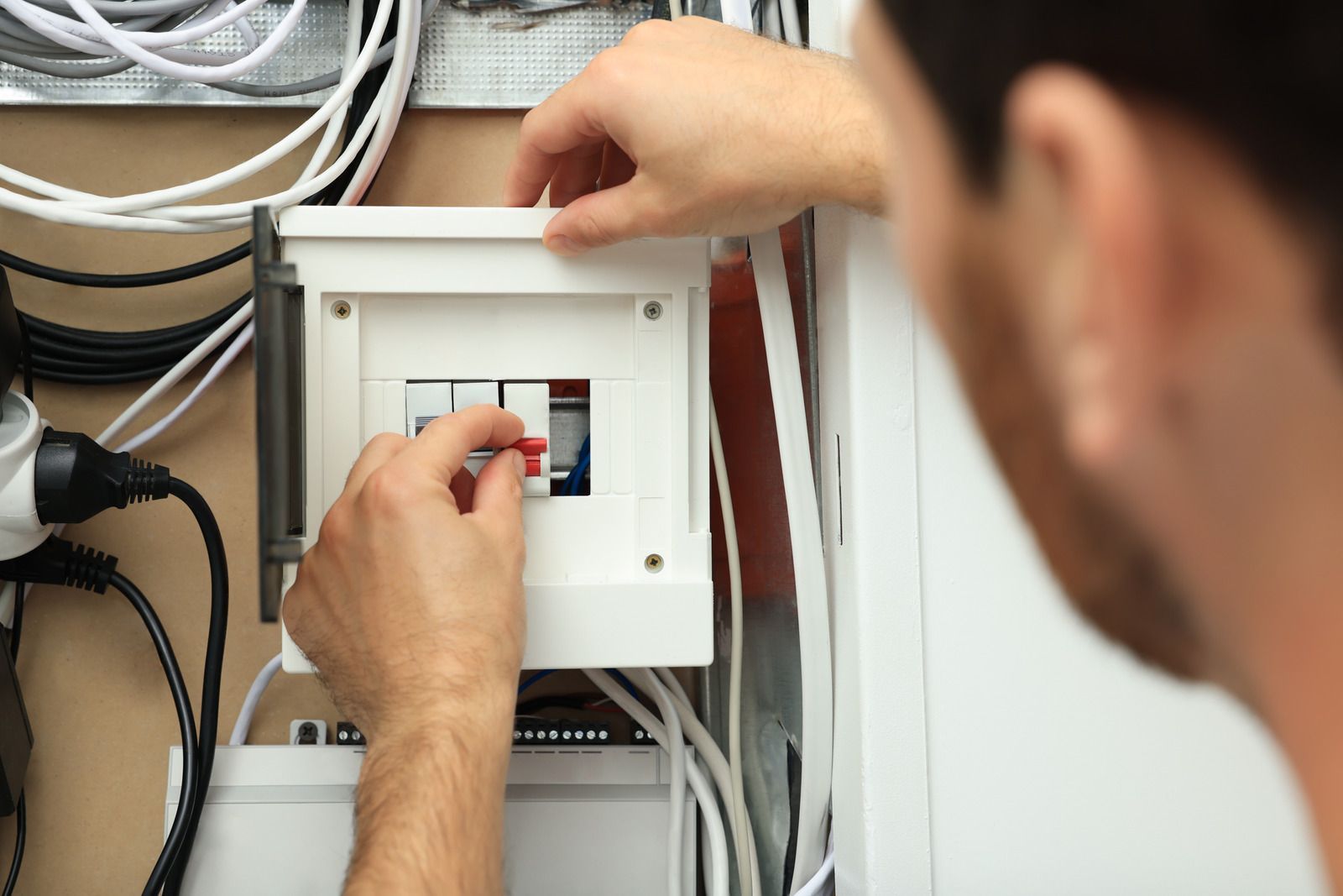 Person flipping a circuit breaker switch in a white electrical panel; wires are visible.