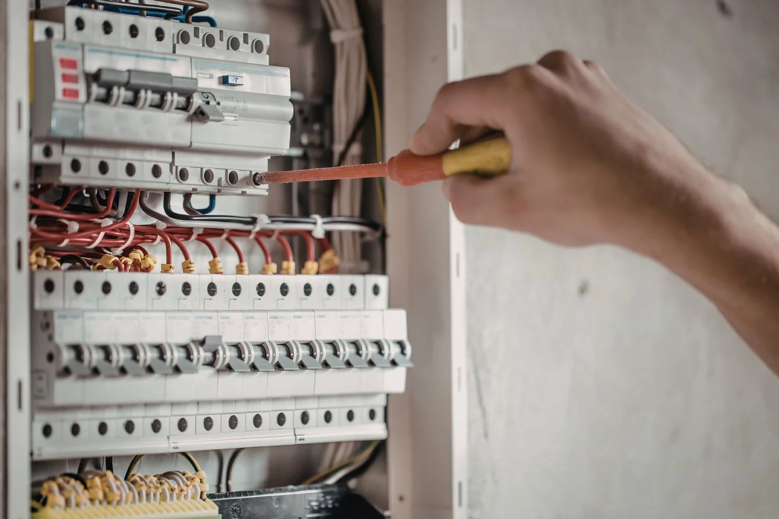 Hand using a screwdriver to work inside an electrical breaker panel with exposed wiring