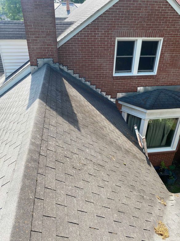 A roof of a brick house with a chimney and a window.