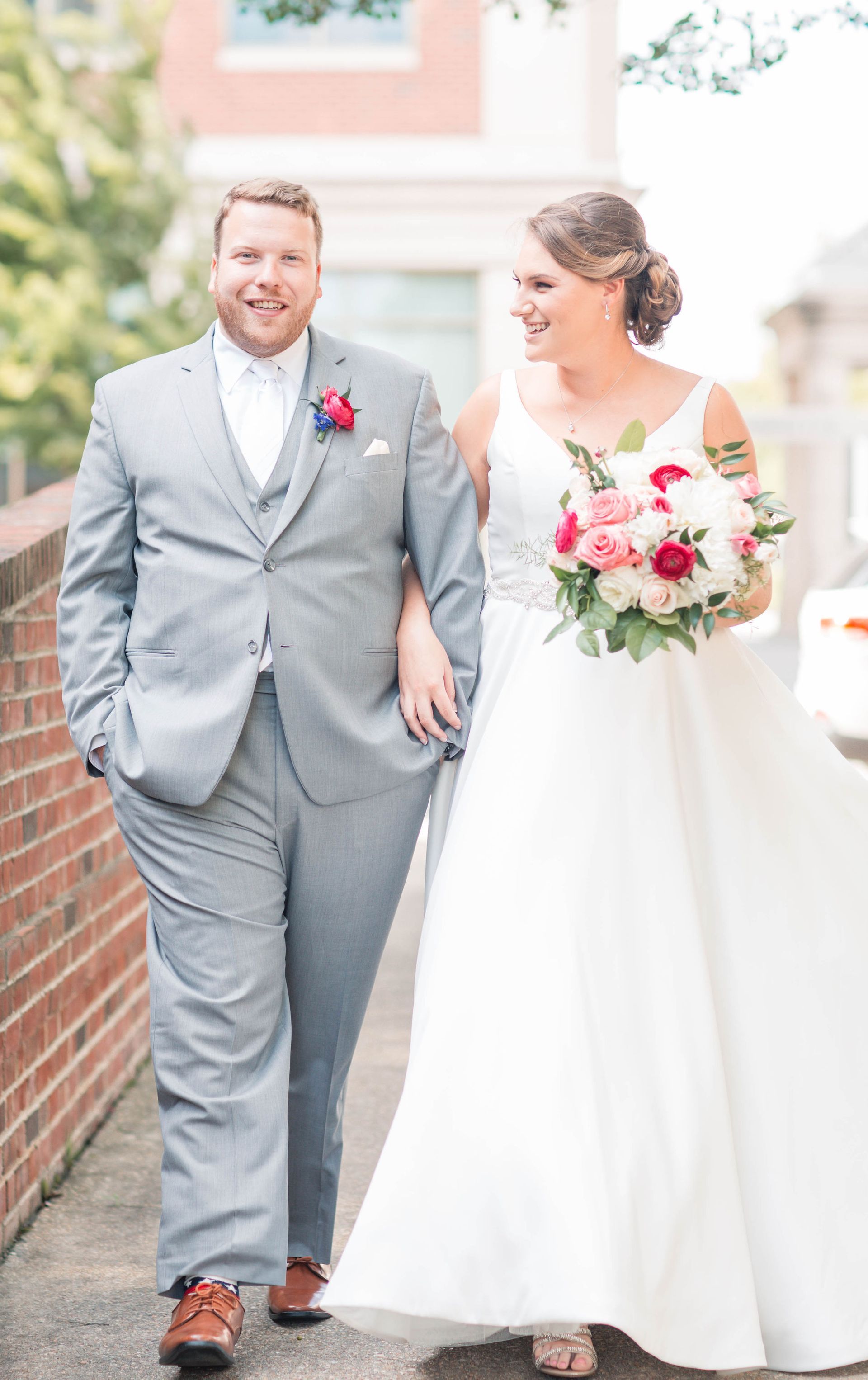 A bride and groom are walking down a sidewalk holding hands.