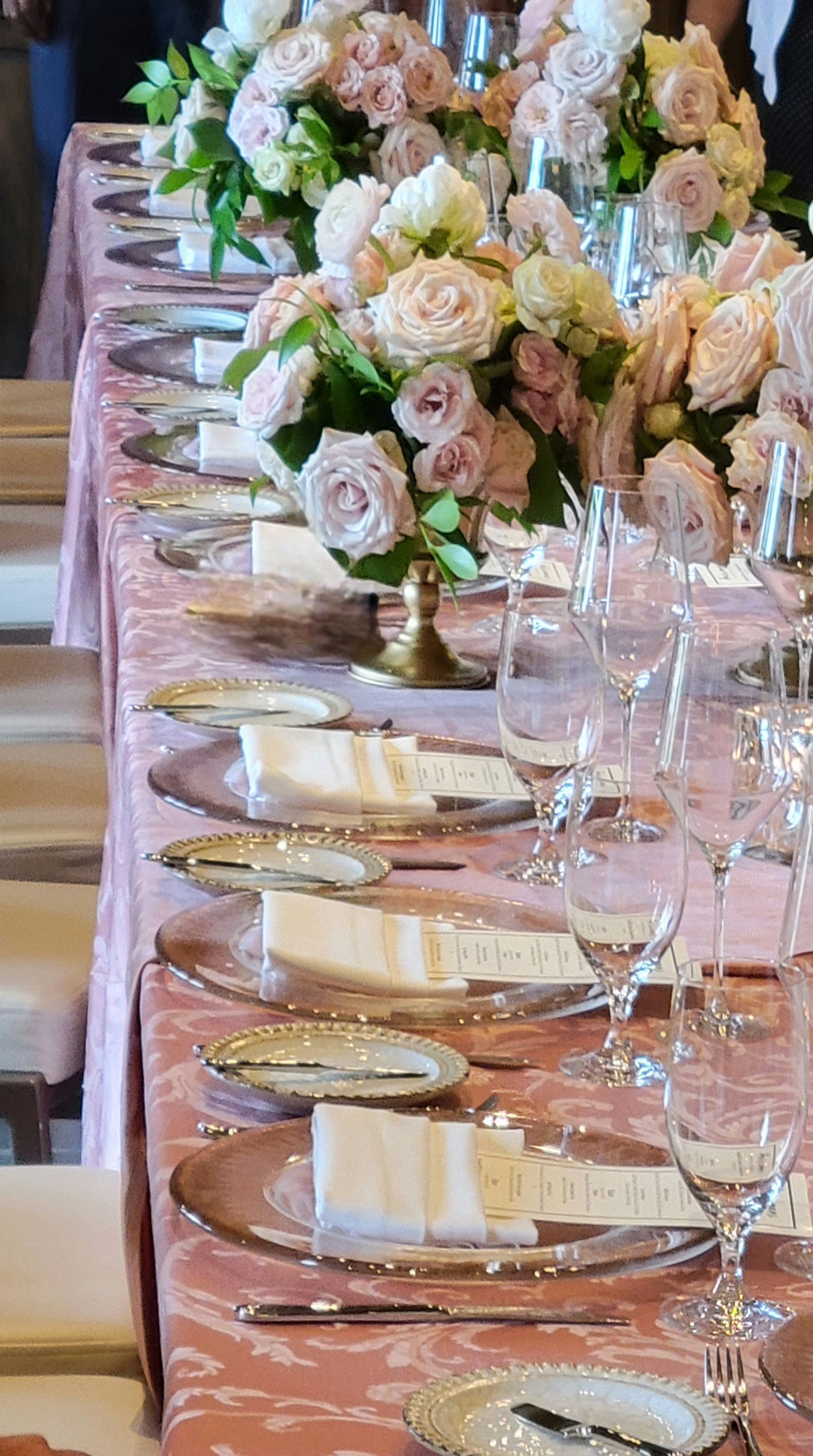 A long table with plates , glasses , napkins and flowers on it.