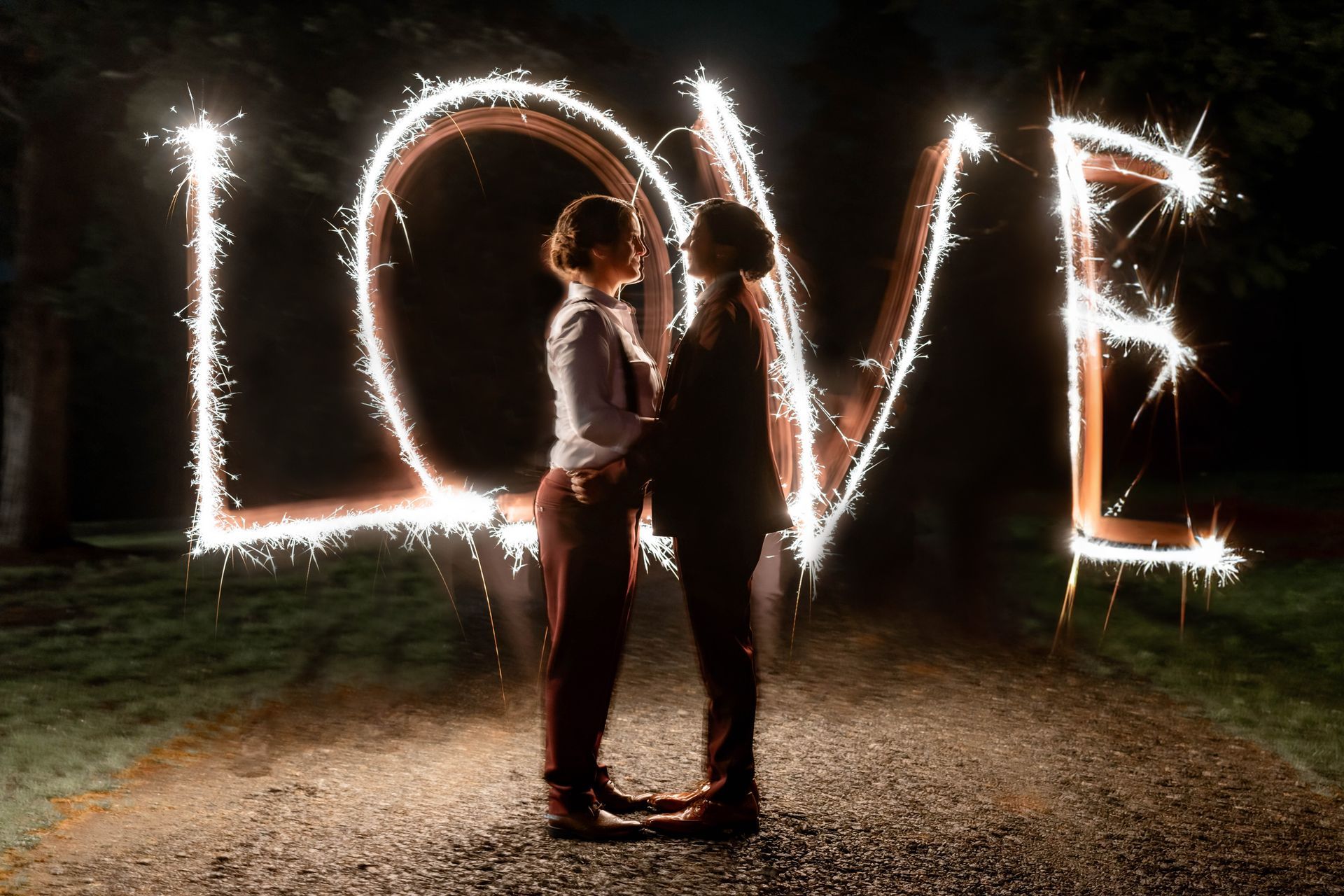 A couple is standing in front of a sign that says `` love '' made of sparklers.