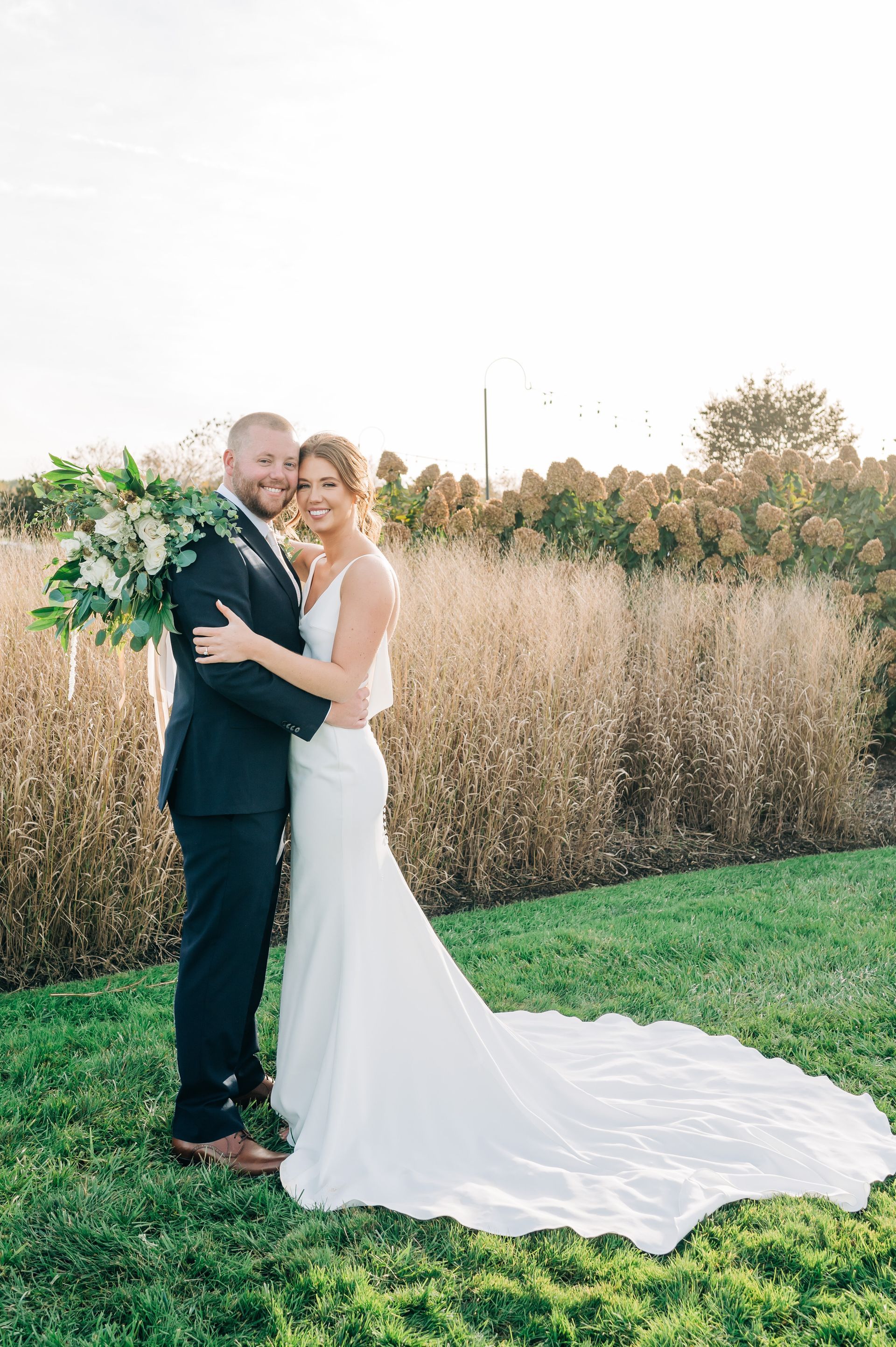A bride and groom are posing for a picture in a field.