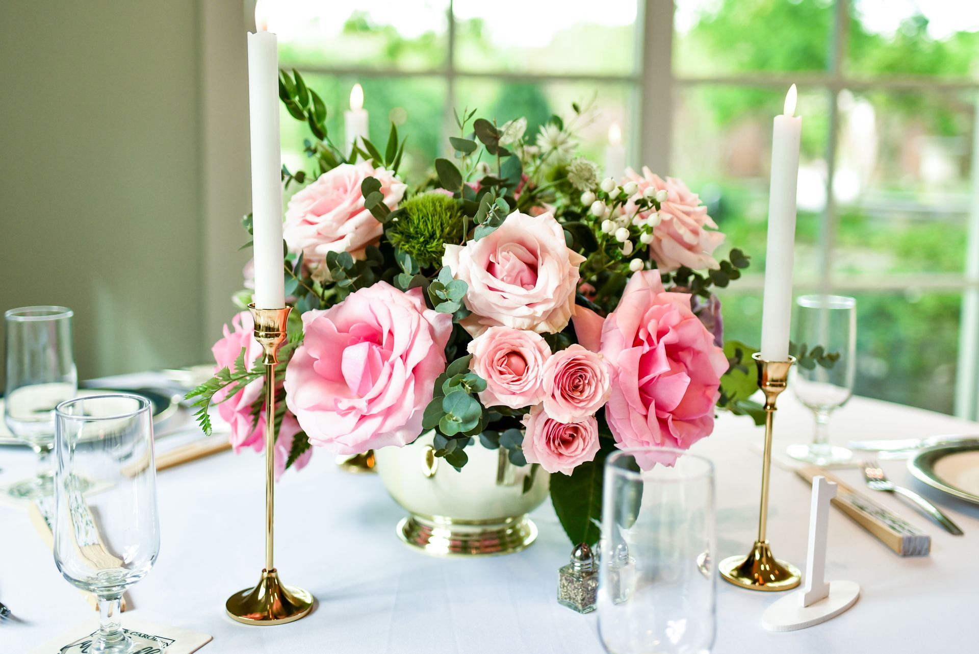 A table with a vase of pink roses and candles on it.