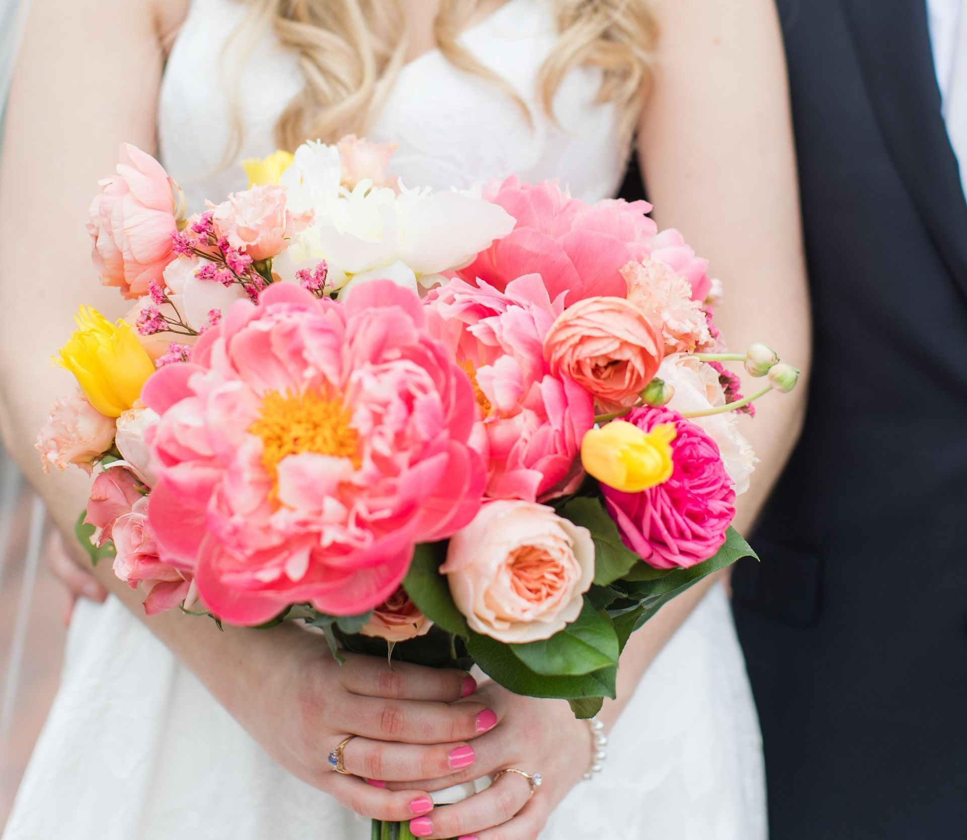 A woman in a white dress is holding a bouquet of pink and yellow flowers