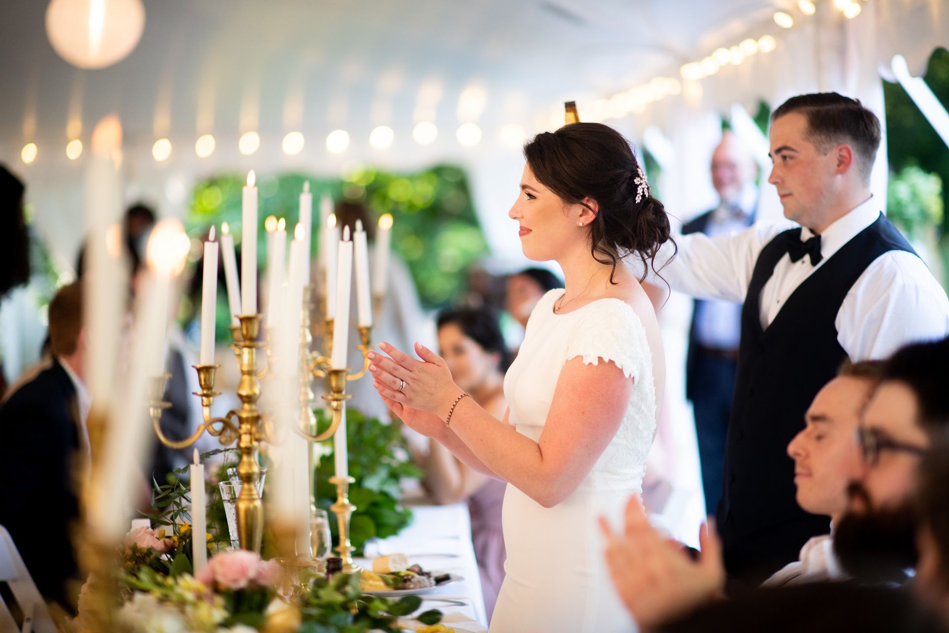 A bride and groom are standing in front of a table with candles.